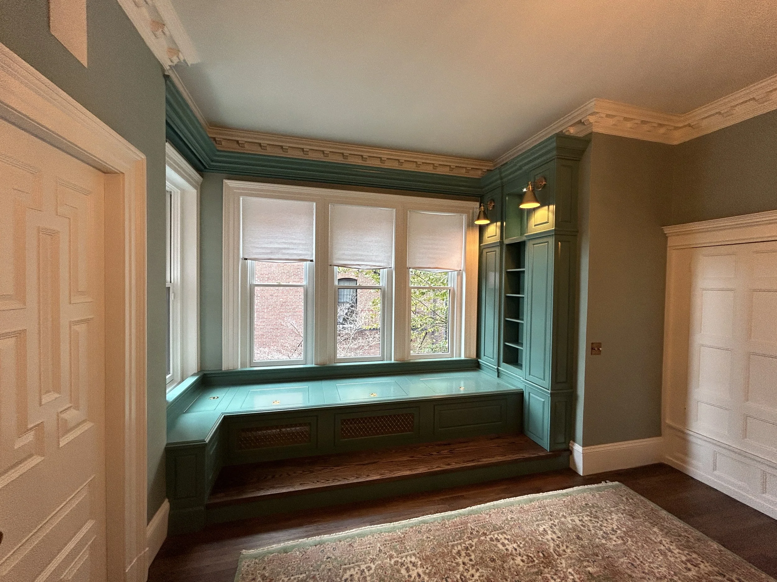 A room with three windows, a built-in window seat with storage, green cabinetry, and white crown molding.