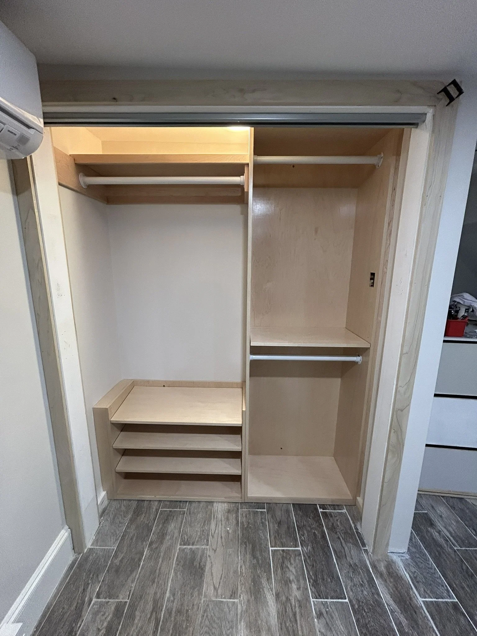 Empty sliding closet with wooden shelves and hanging rods, located in a room with wood-look tile flooring.