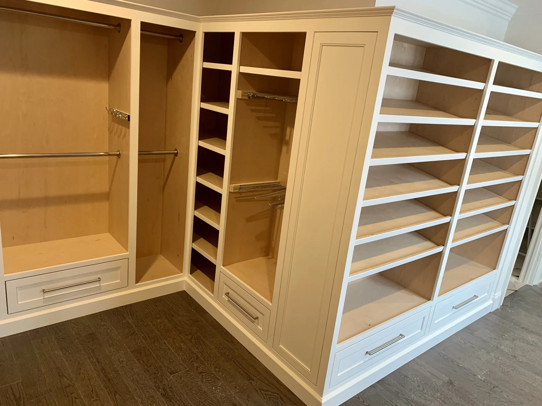 Empty custom white built-in closet with multiple shelves, drawers, and hanging rods.