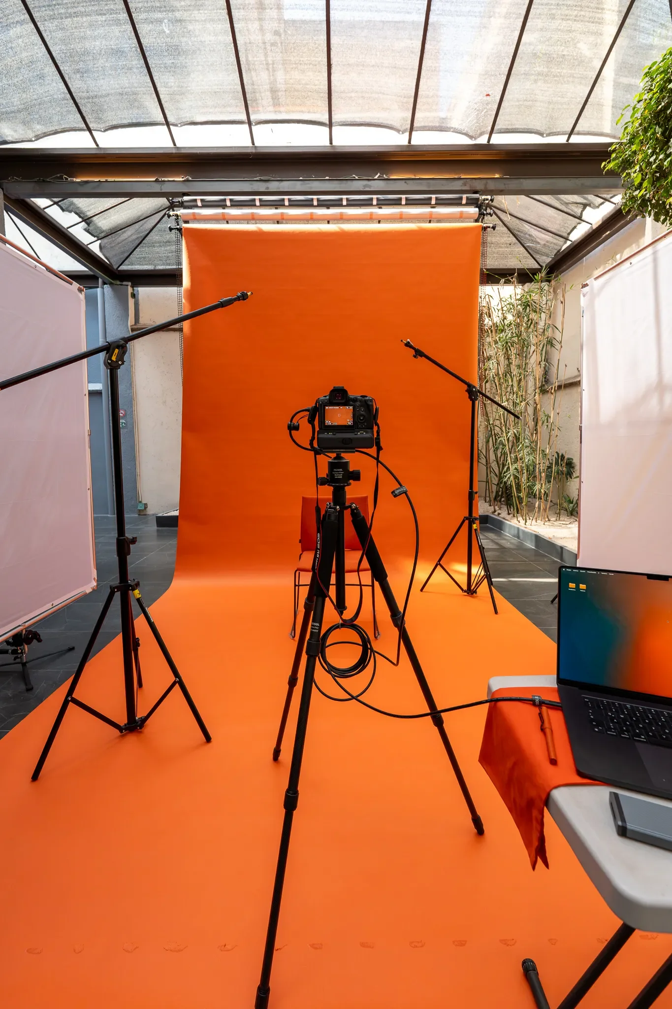Estudio fotográfico con fondo de tela naranja, cámara en trípode, luces y equipo de grabación.