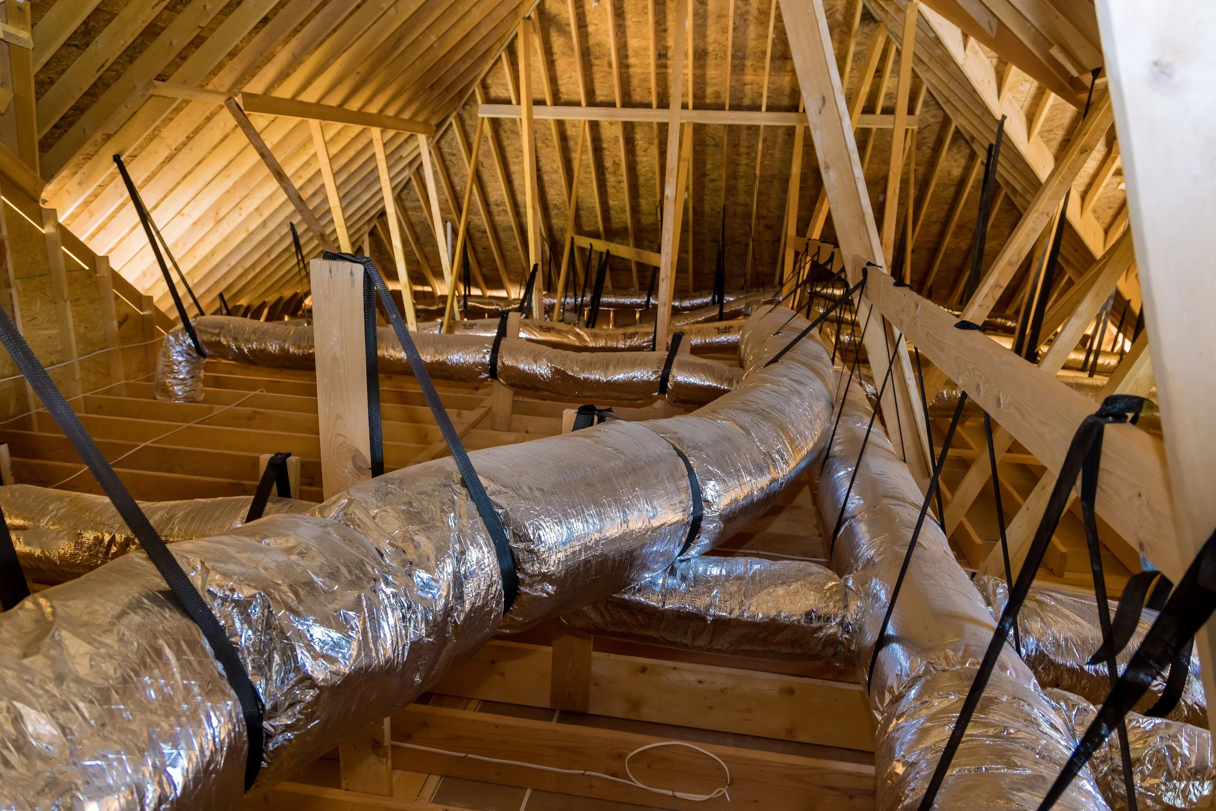 Attic space with wooden framing, insulation-covered air ducts, and ventilation straps.