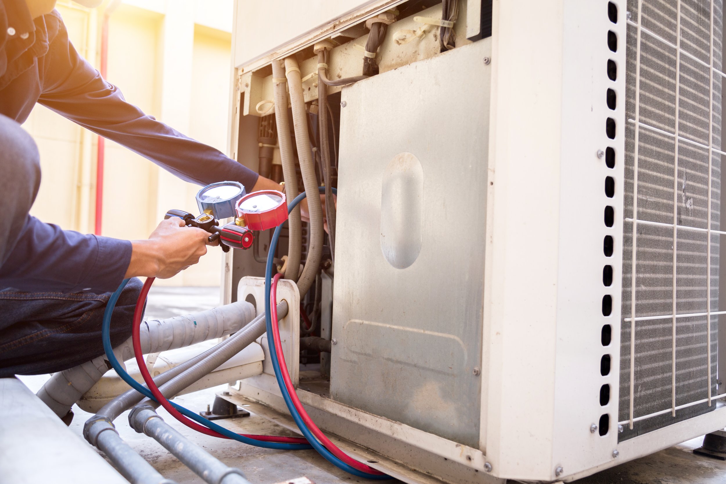 Technician measuring the refrigerant pressure in an air conditioning unit with gauges connected to the system.