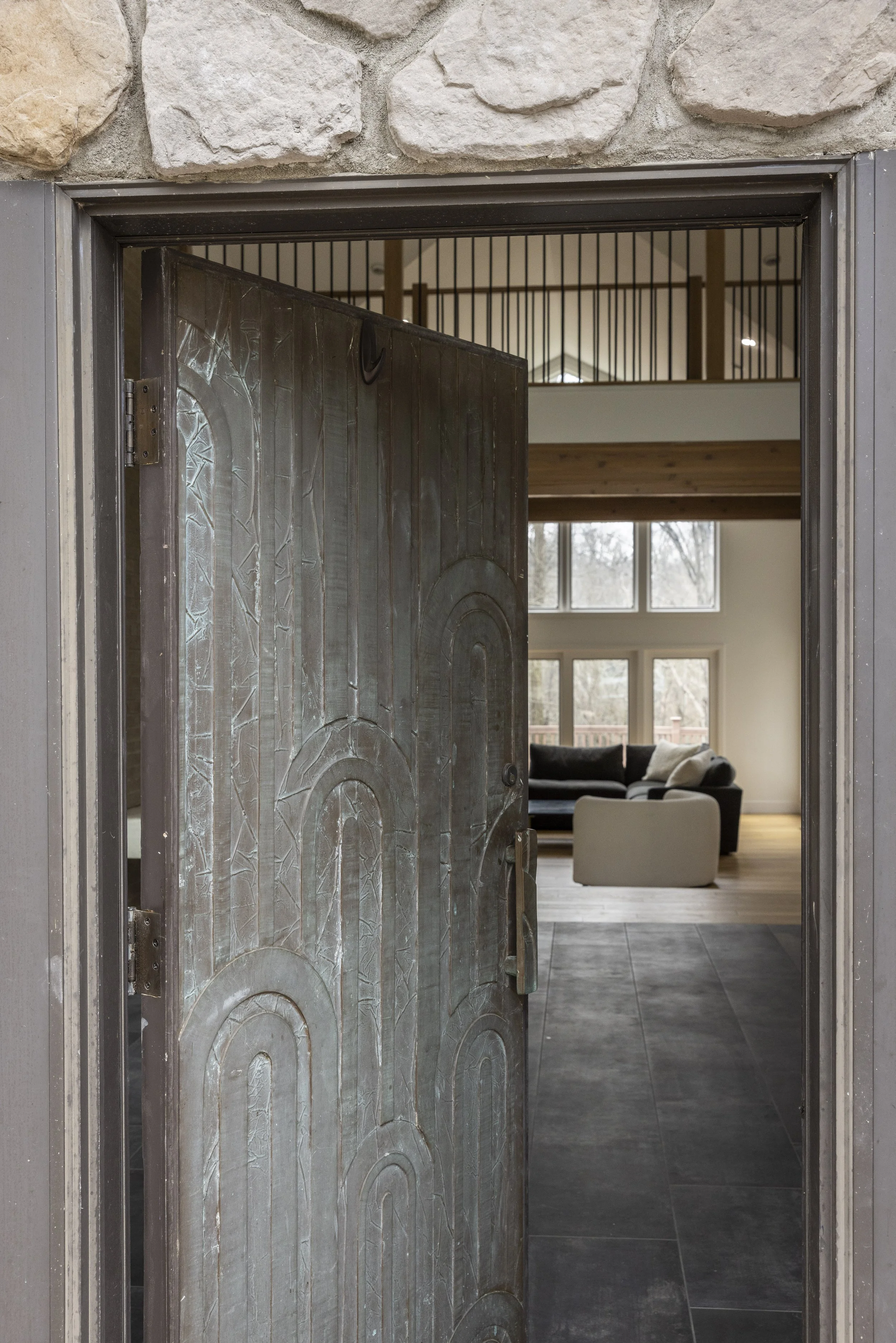 A metal door slightly open, revealing a living room with large windows, a black sofa, and a white armchair.