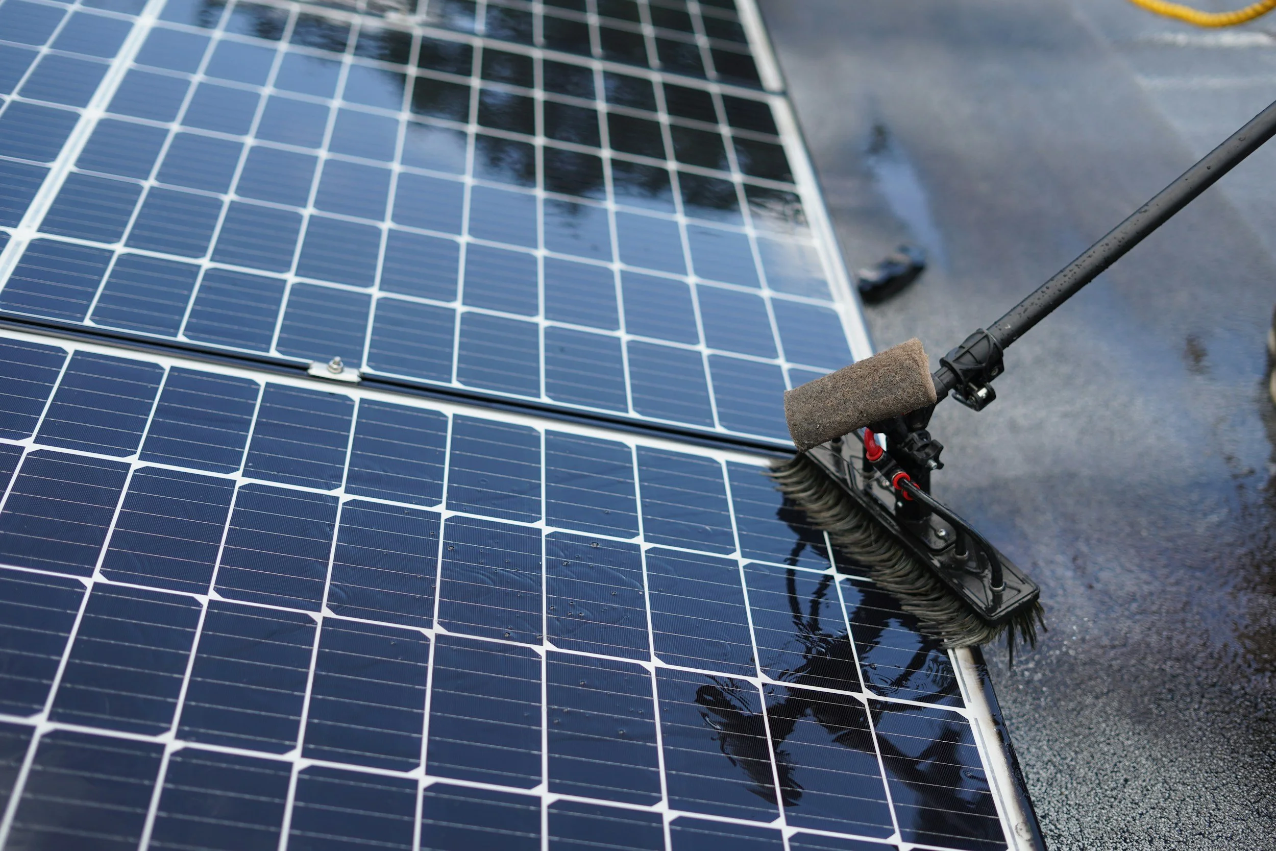 Close-up of solar panels being cleaned with a brush, wet surface on a rooftop.