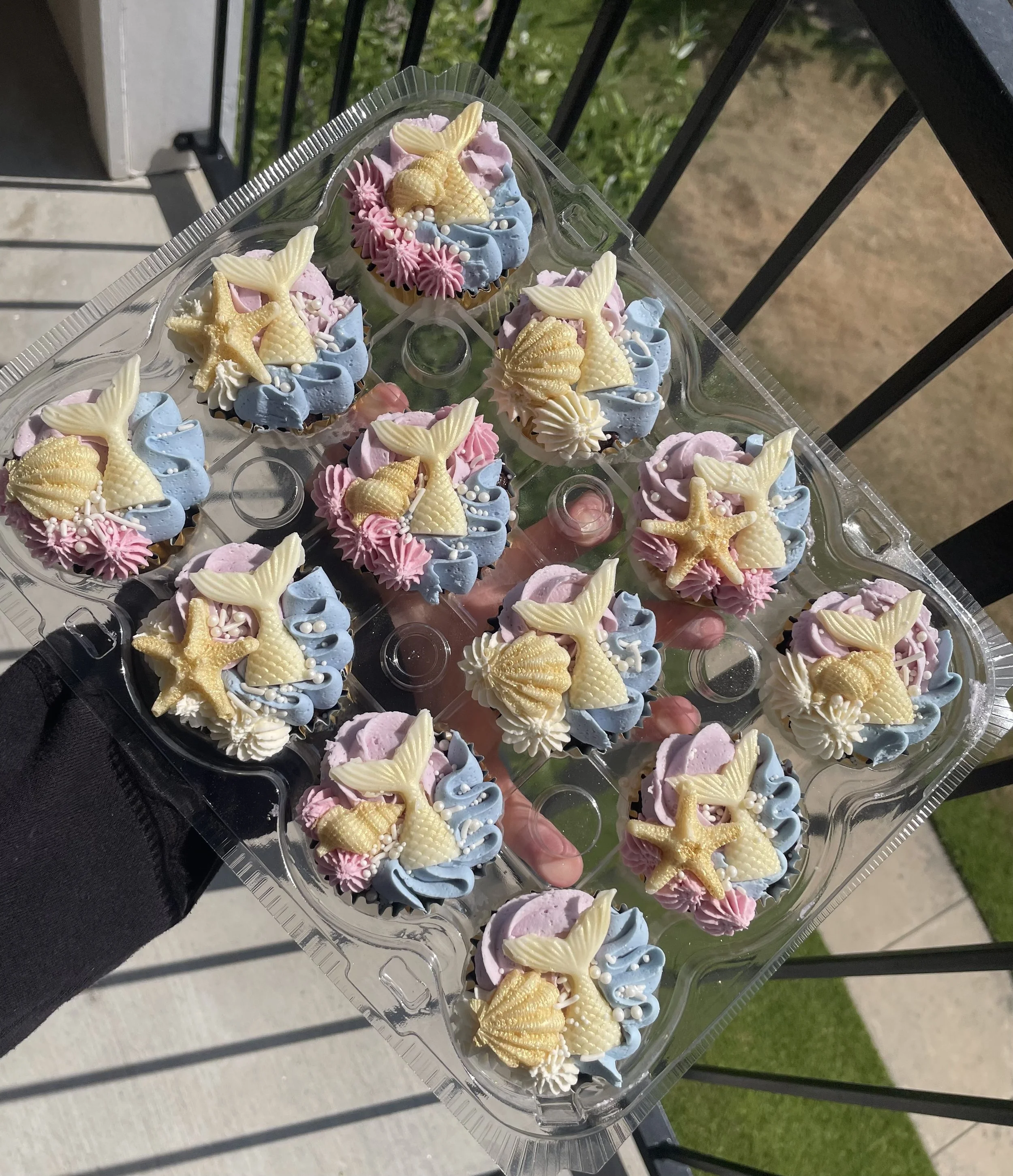 Tray of cupcakes decorated with pastel pink, blue, and white frosting, topped with starfish and seashell-shaped fondant decorations.