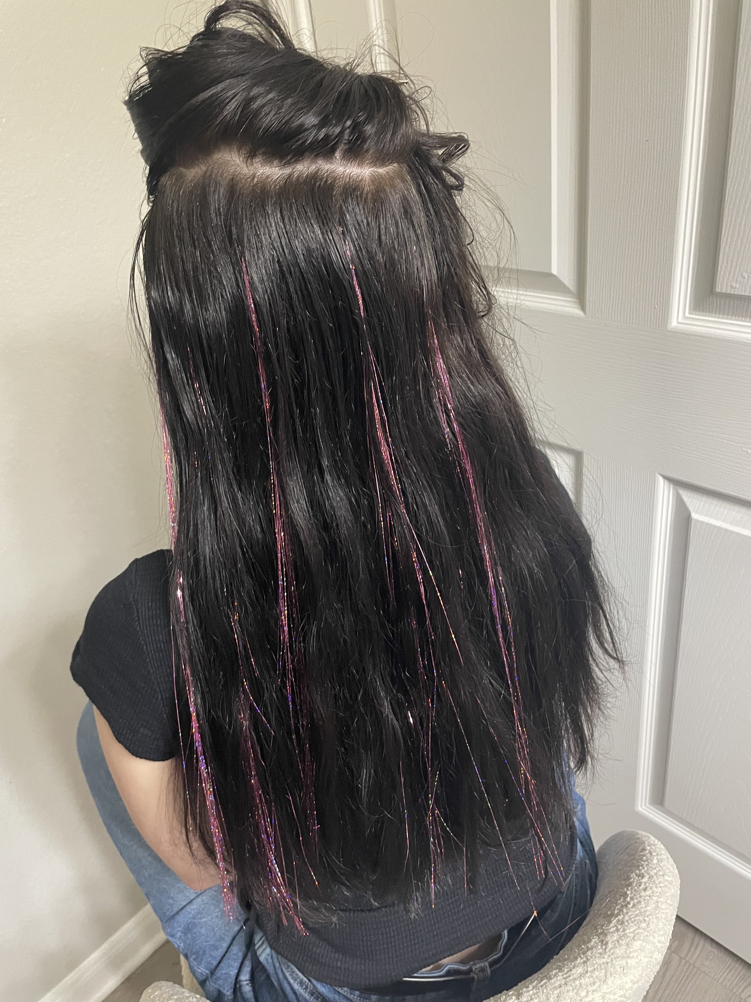 Person with long, dark, wavy hair with colored streaks sitting near a door.