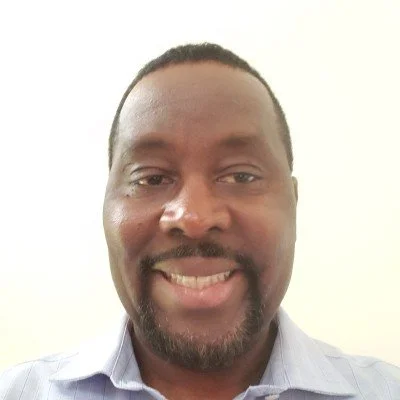 A man smiling in a light-colored collared shirt with a light background.
