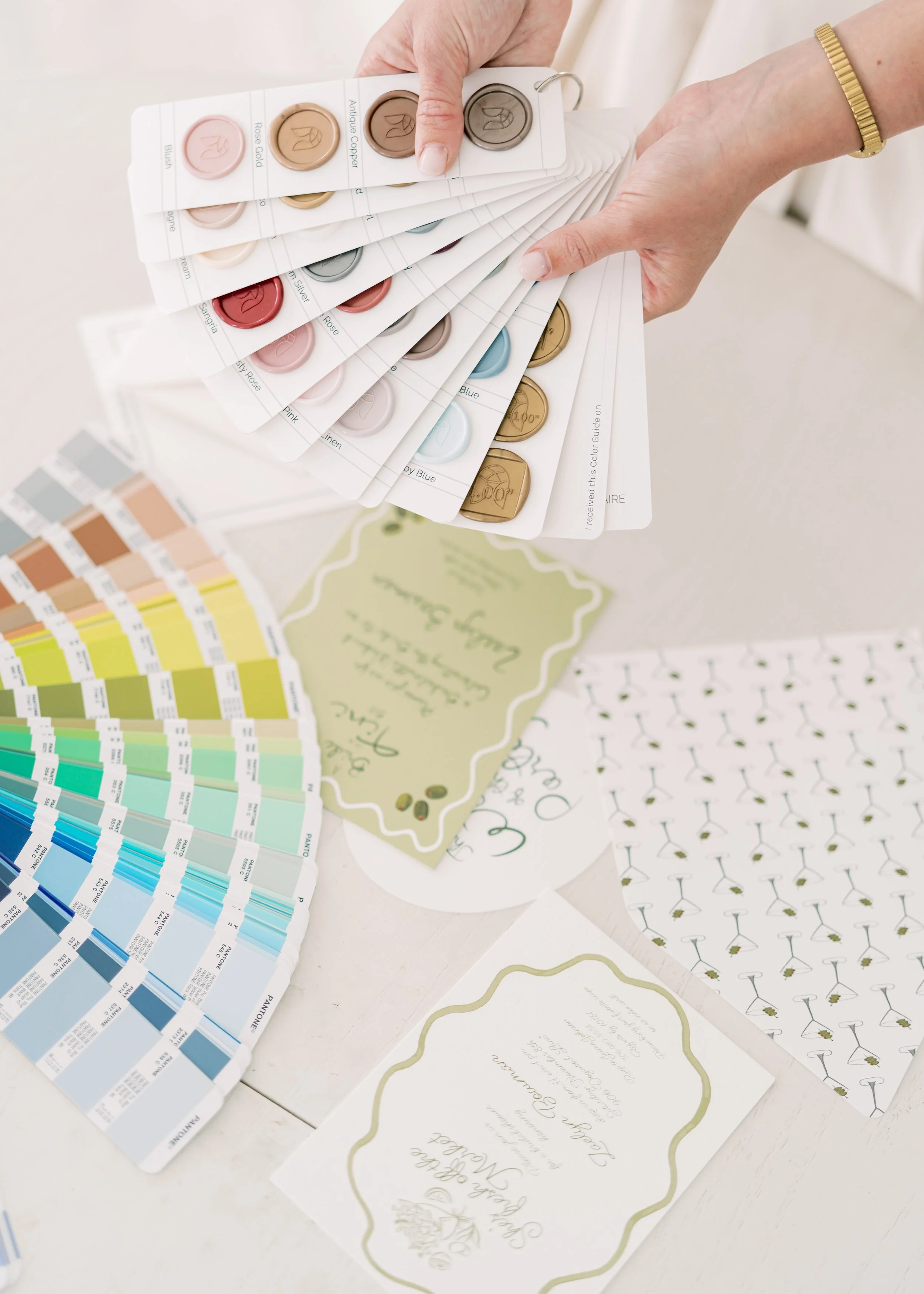 A person holding color swatches with paint chips, surrounded by color sample cards and printed booklets on a white table.
