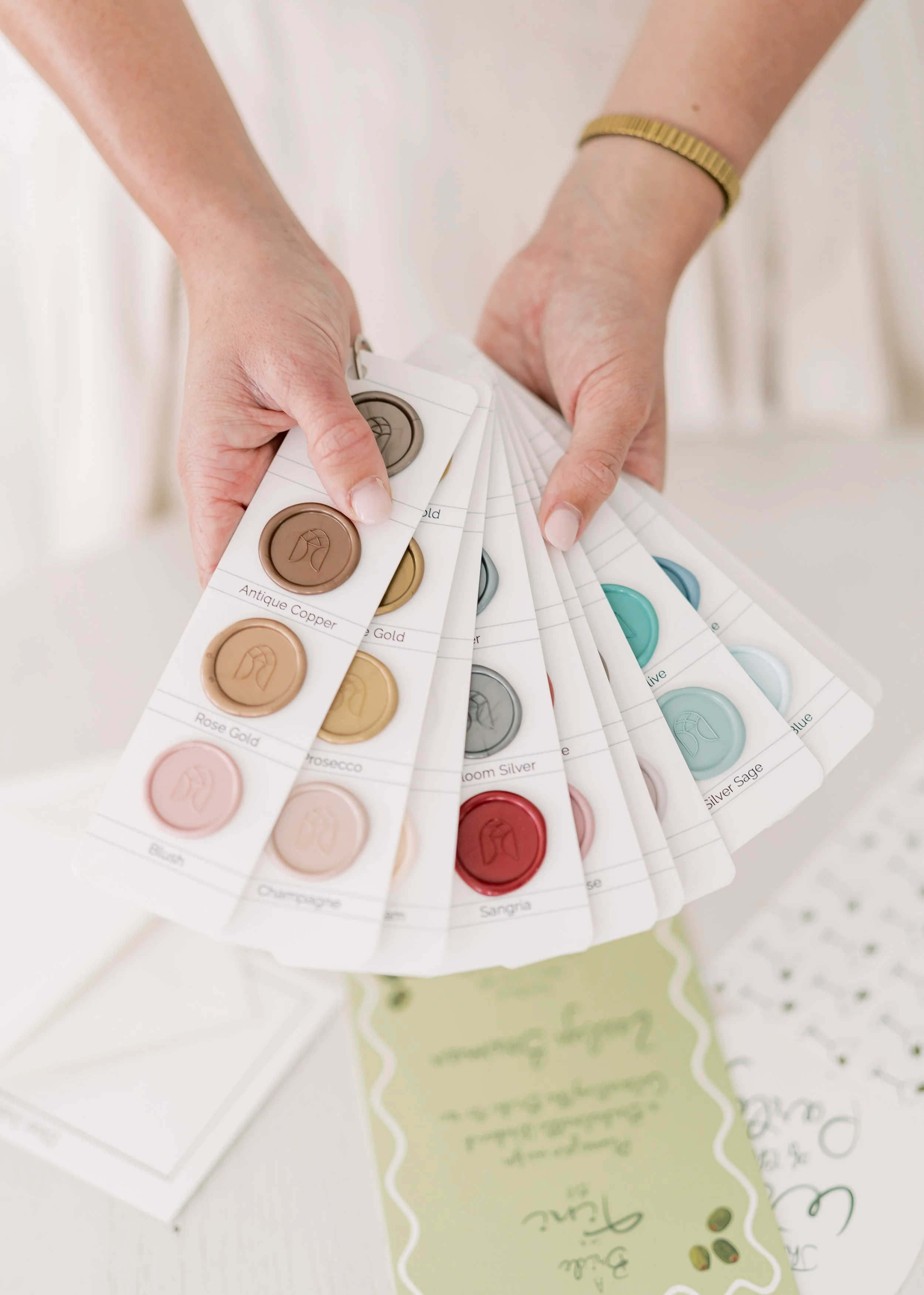 Person holding color sample cards with various shades of paint or ink, including names like Antique Copper, Rose gold, and Sangria.