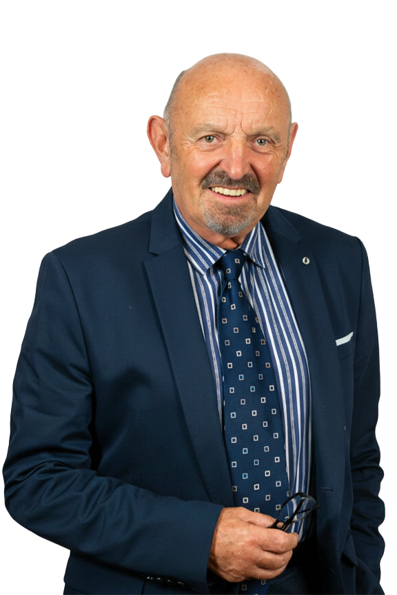 An older man in a dark suit and striped blue shirt, smiling and holding glasses, posing against a black background.