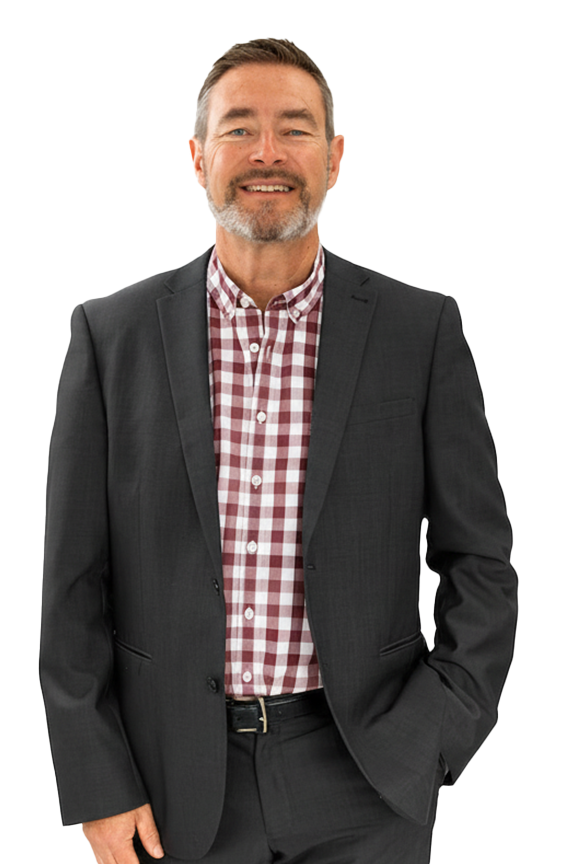 A smiling middle-aged man with a beard, dressed in a dark suit and a red and white checkered shirt, standing against a plain background.