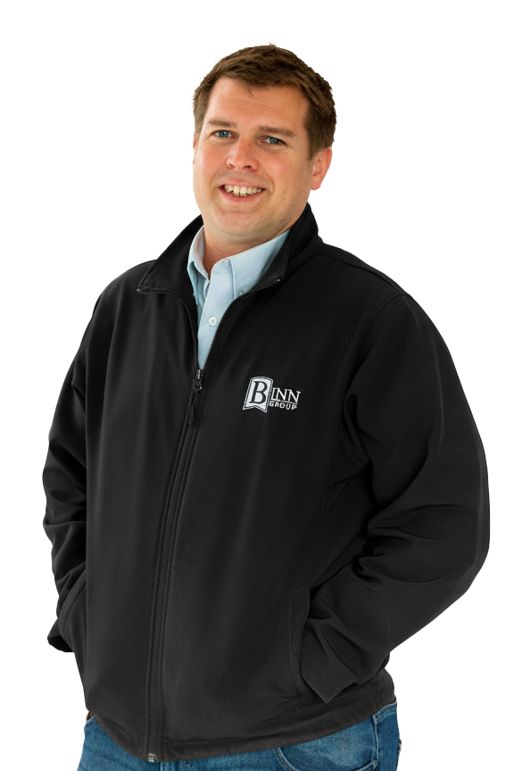 A man smiling, wearing a black jacket with a logo on the left chest that reads 'Binn Group,' and a light blue collared shirt underneath.