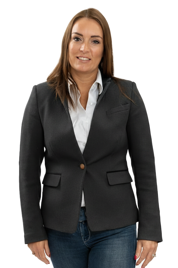 A woman with long brown hair wearing a black blazer over a white shirt and blue jeans, standing and smiling.