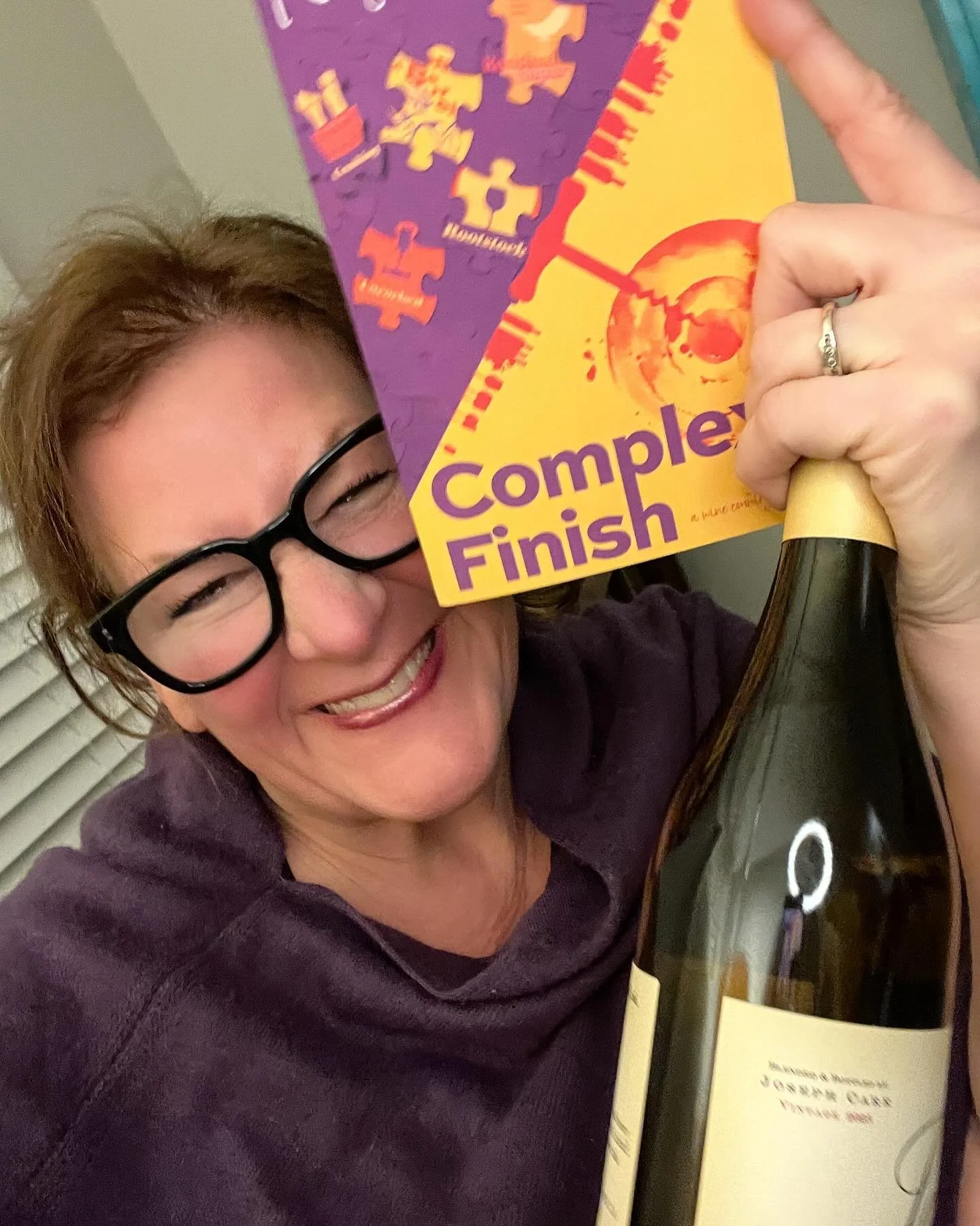 A woman wearing glasses, smiling, holding a book, Complex Finish by Kelly Kay - A Winery Romance Series