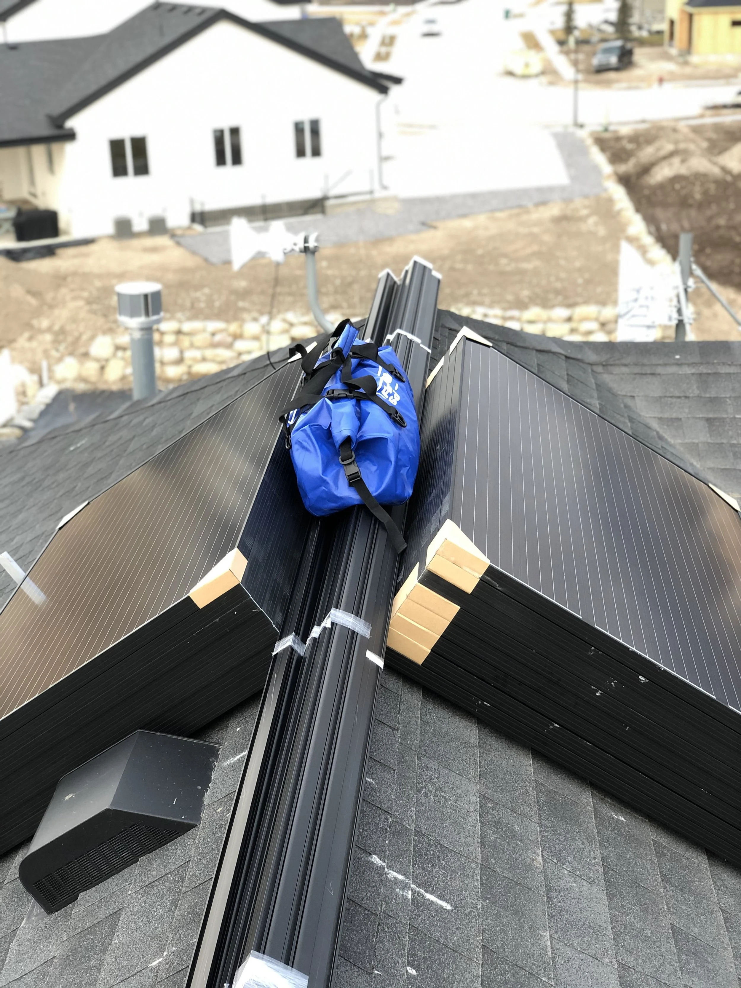 Tools and materials on a house roof, with a blue bag placed among metal roof panels and a green ventilation turbine visible in the background.