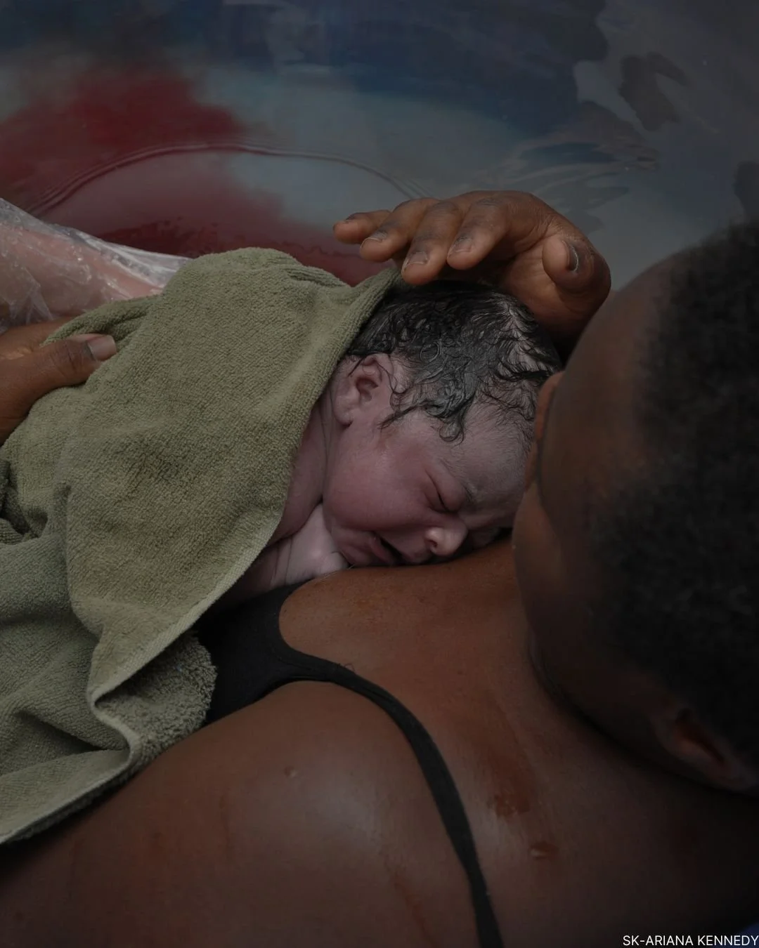 A woman giving birth in a medical setting with assistance from healthcare professionals, a newborn baby being delivered.