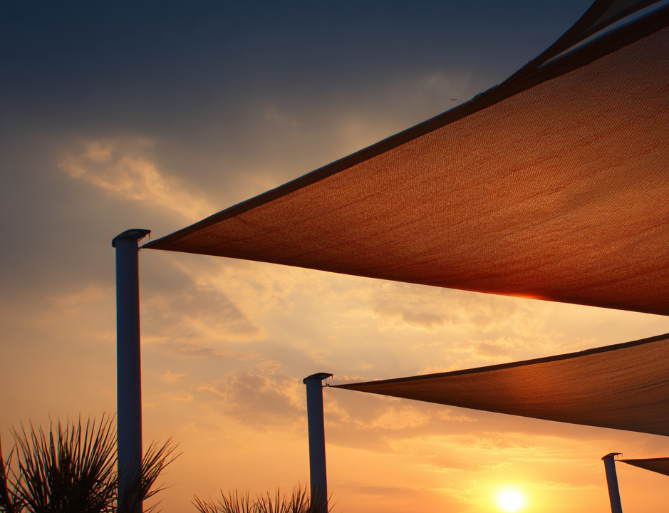 An image of shade sails in an afternoon sunset. The shade sails are brown tan attached to metal posts. Heavy Duty.