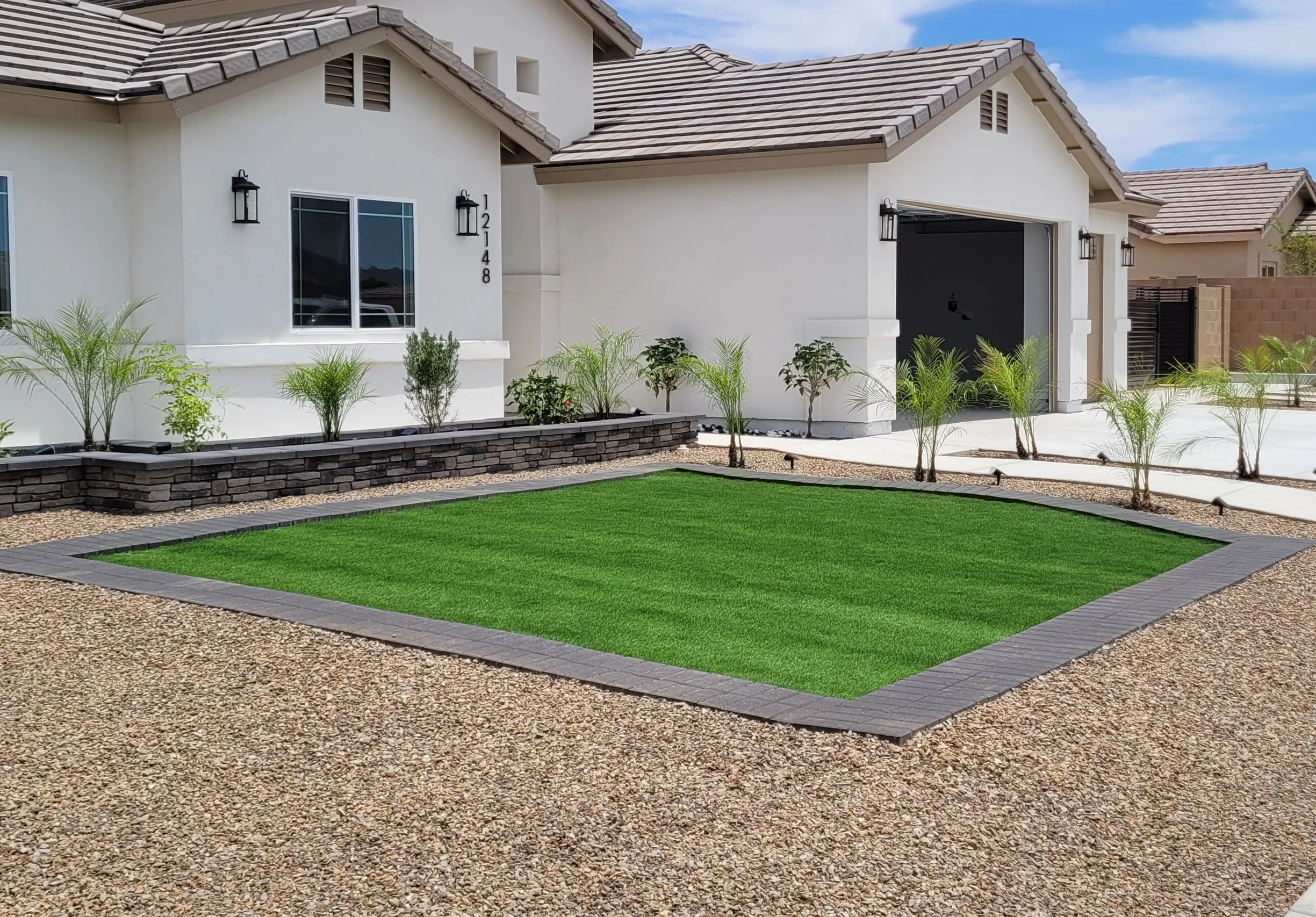 Turf installed by Arizona Quality Landscaping Company, LLC. It is lush, green, and is maintenance free. The border has double pavers by Belgard in the Graphite Color. There are also many plants surrounding the turf and a modern gray retaining wall.