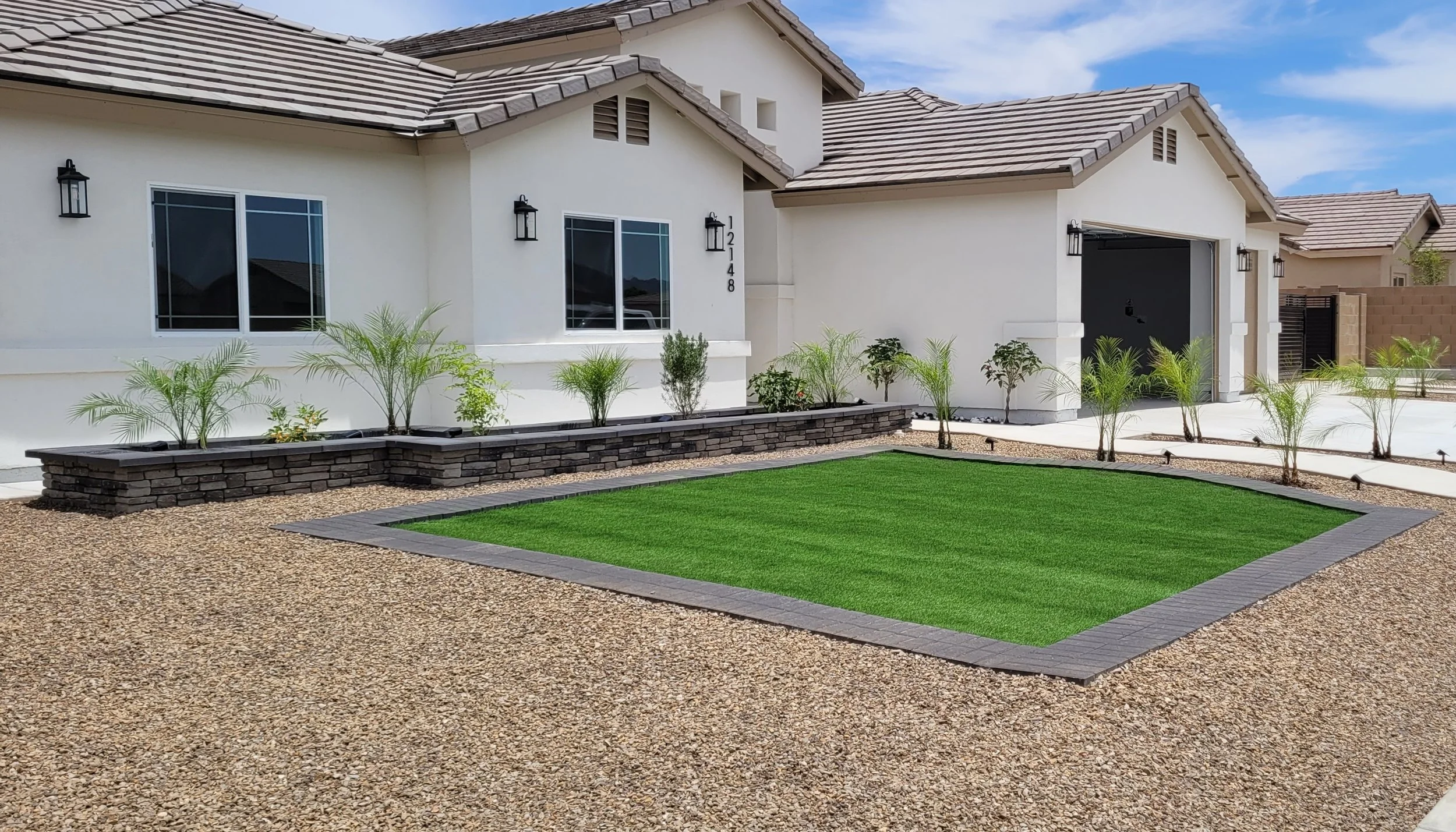 A new home build in Arizona with artificial turf, double edged pavers, a retaining wall planter, beautiful decorative rock, and solar lighting. The plants are healthy and are on an automated watering timer.