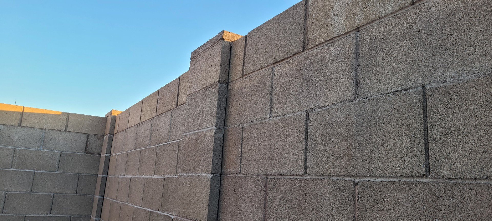 A brown tan wall that has been raised by one course, or level, helping to promote privacy and security. The new addition is cohesive with the wall that was already installed.