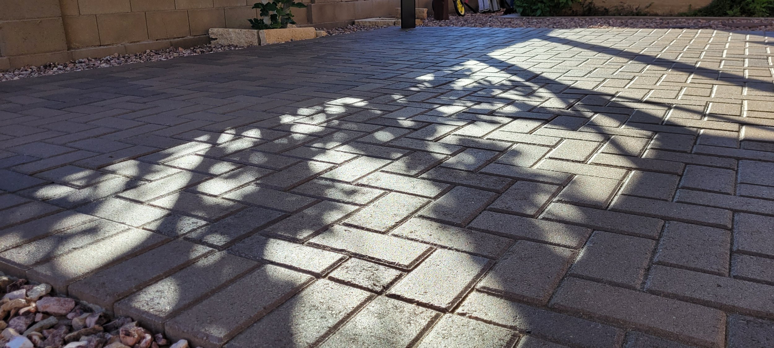 Concrete pavers in a herringbone pattern. There is a planted fig in the rear with more decorative rocks installed by a landscaping contractor professional. The pavers are sealed with a satin finish and are in purple, brown and tan hues.