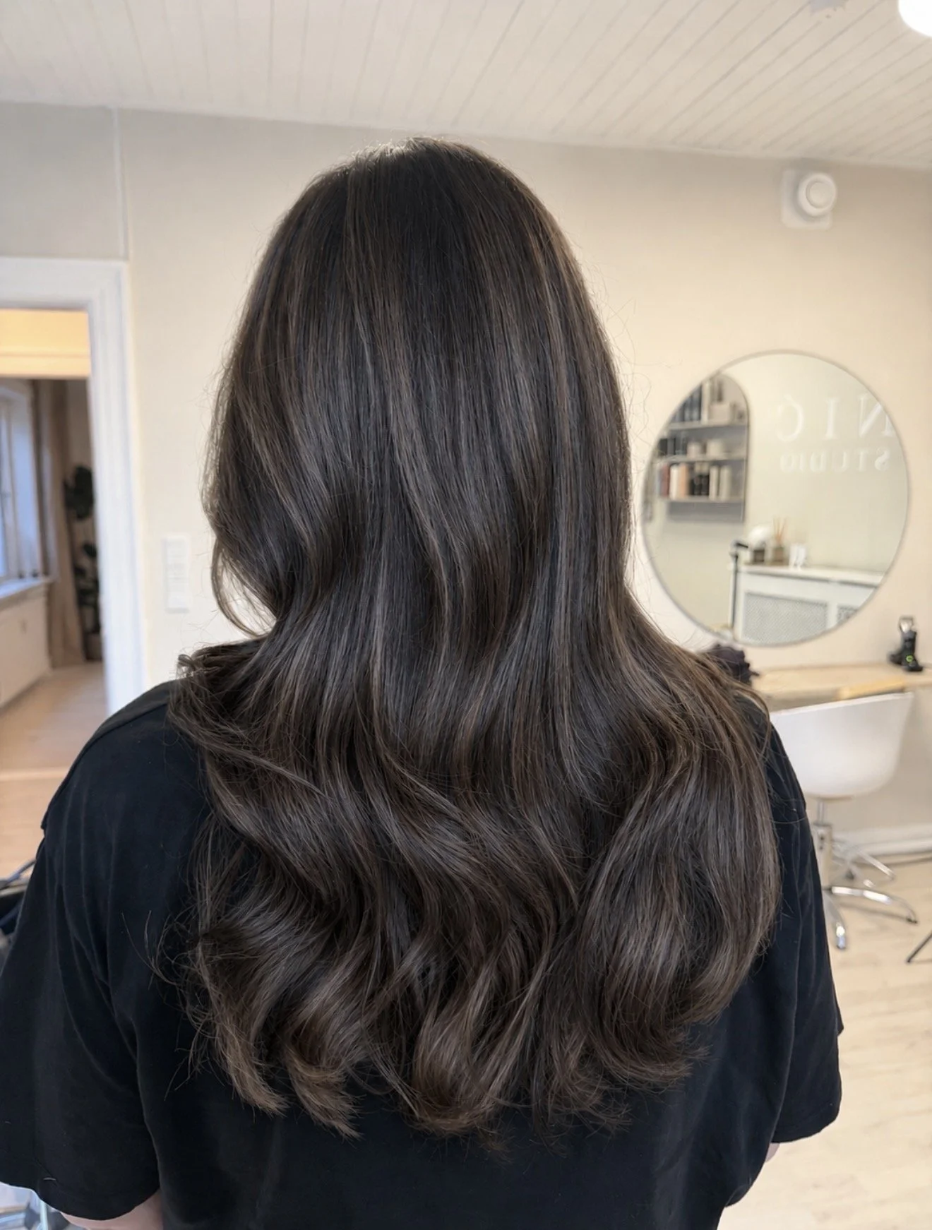 Billedet viser en person med lang, mørkebrunt hår, set bagfra i en frisørsalon.