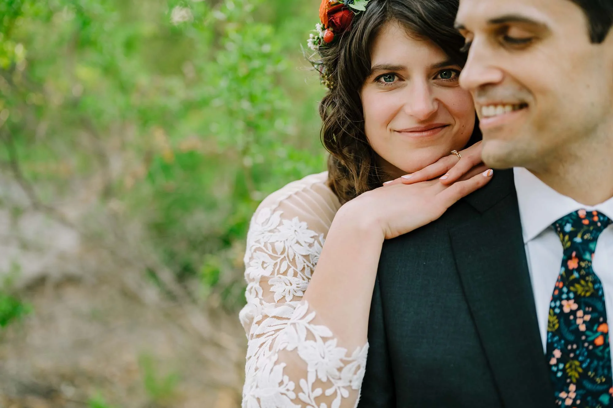 A woman with a floral headband resting her hand on a man's shoulder, both smiling, outdoors with green foliage in the background.