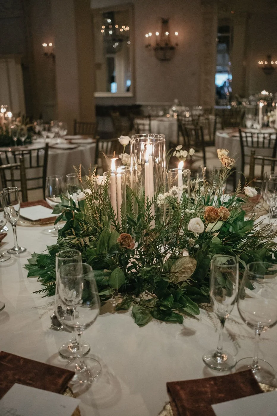 Elegant banquet table with floral centerpiece and lit candles in a softly lit room.
