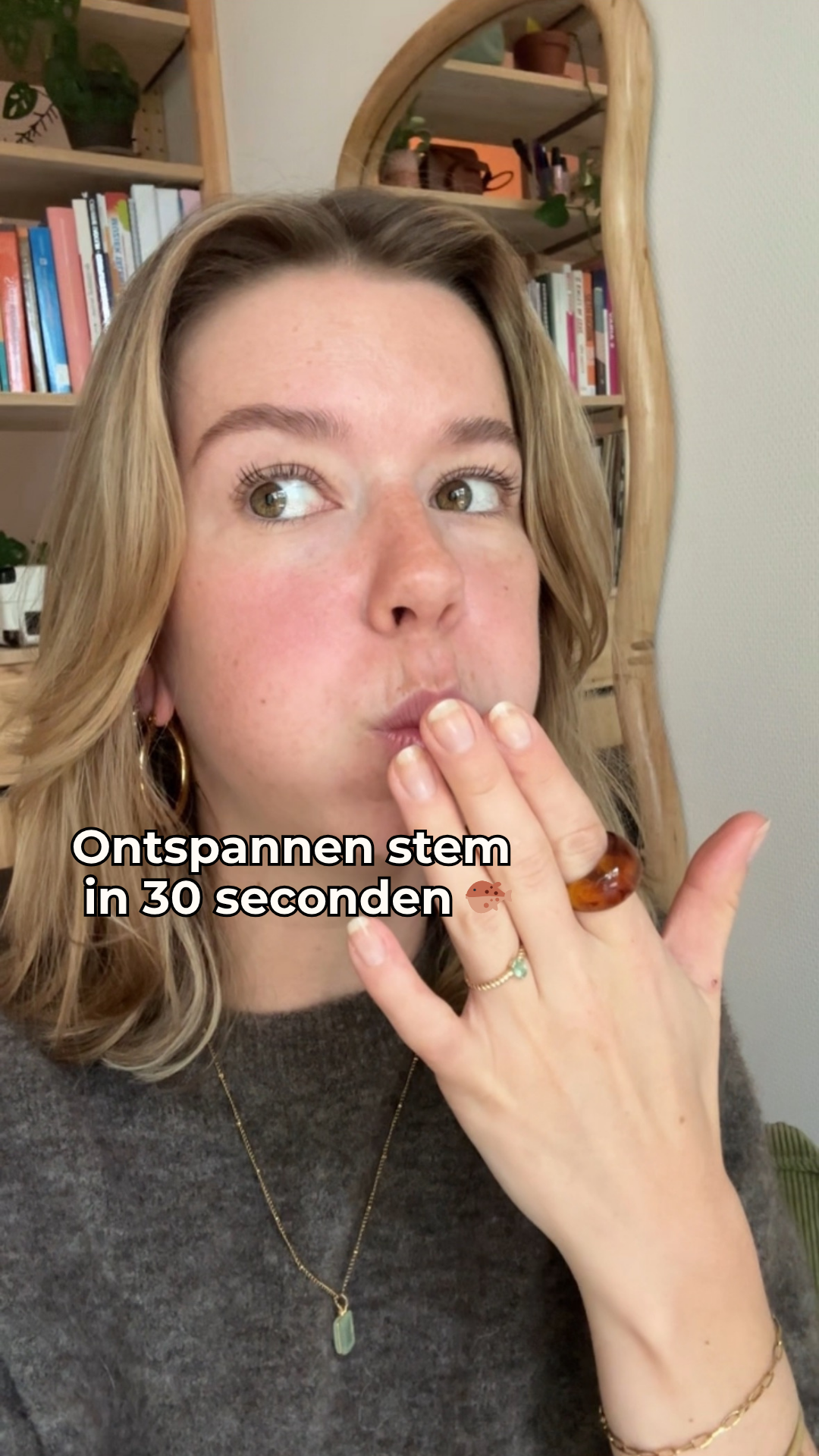 Vrouw met hand voor mond die ontspannen stem in 30 seconden aanbeveelt, achter een boekenkast en ronde spiegel.