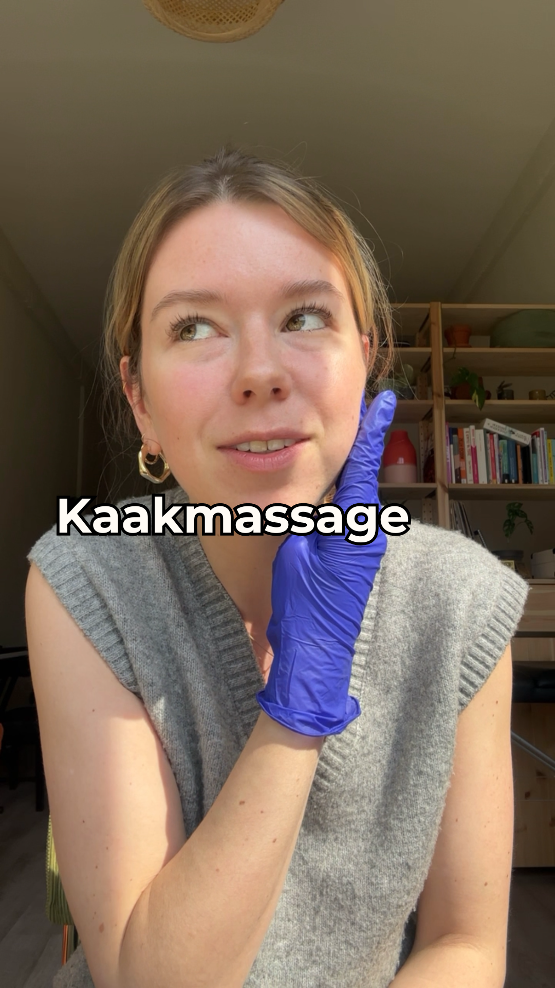 Een vrouw krijgt een nekmassage van een persoon met een blauwe handschoen, de achtergrond laat een kamer met boekenplanken zien.