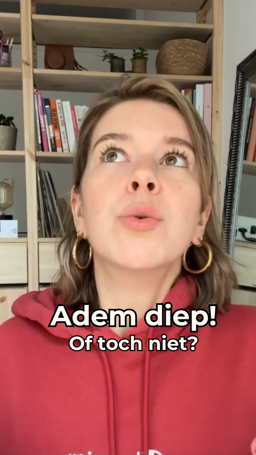 Vrouw met bruin haar en grote gouden oorbellen, draag een rode hoodie, kijkt omhoog, achtergrond met boekenplanken, tekst: 'Adem diepd! Of toch niet?'
