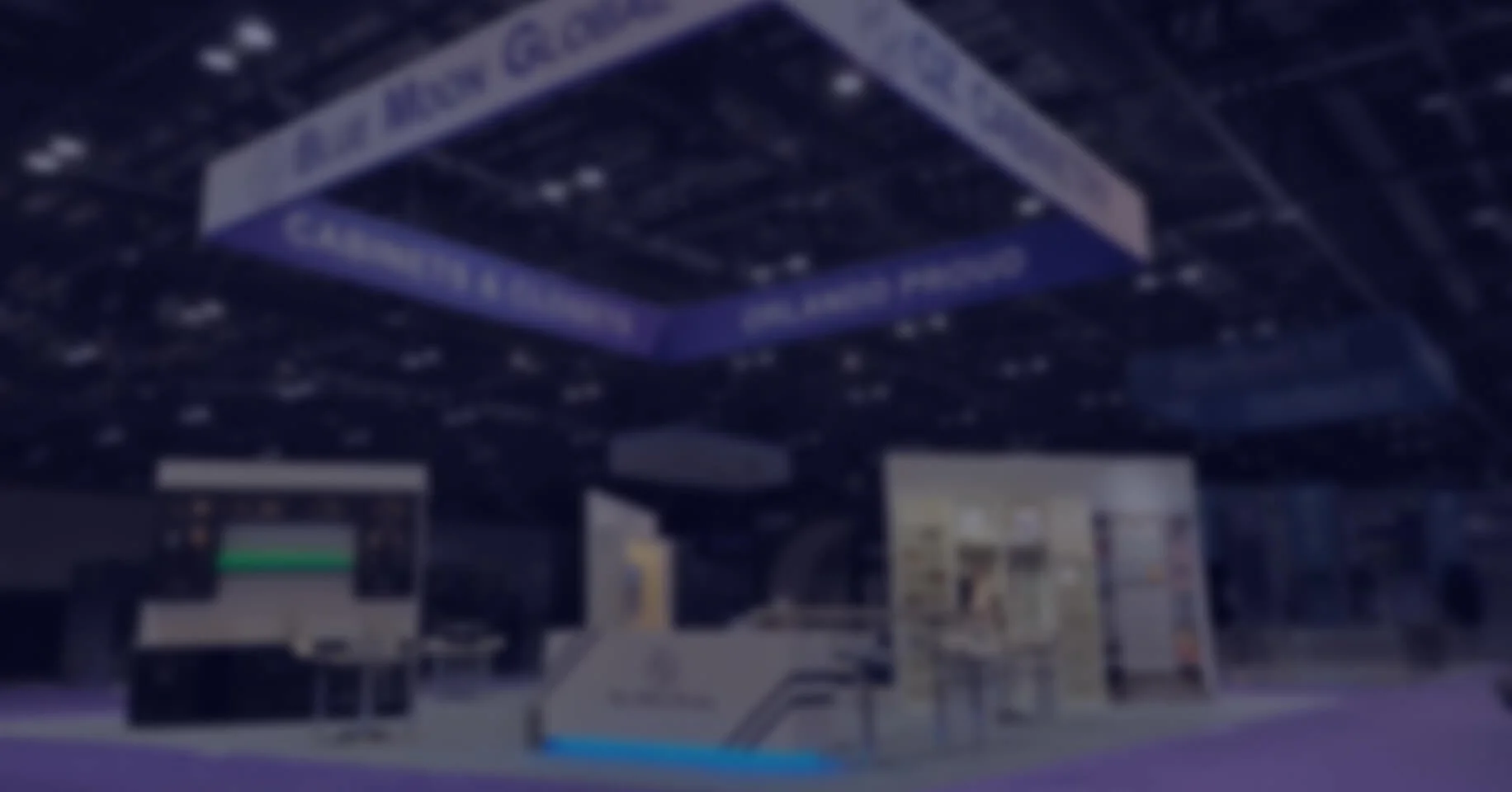 Behind-the-scenes shot of the Facebook GBC event at a convention hall with a large hanging sign, a check-in booth, and information displays, under dark lighting with blue accents.