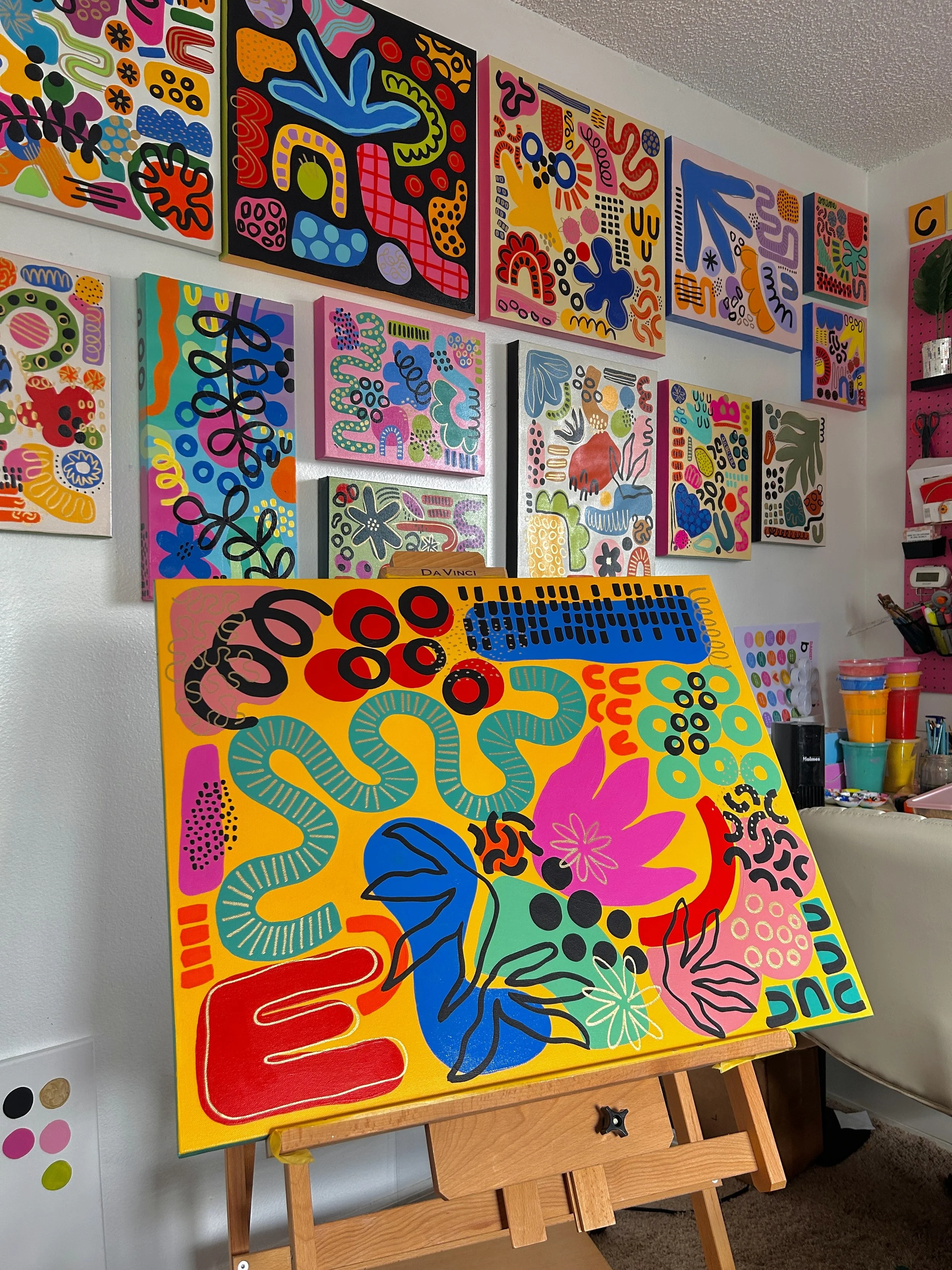 Colorful abstract painting with various organic shapes and patterns on a canvas on an easel.