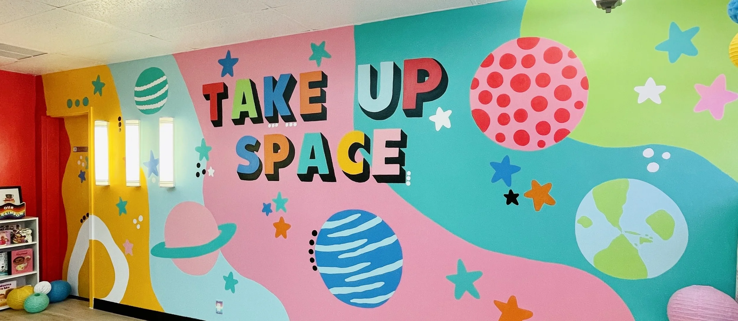 Colorful mural with planets, stars, and the phrase 'Take Up Space' in bold, colorful letters.