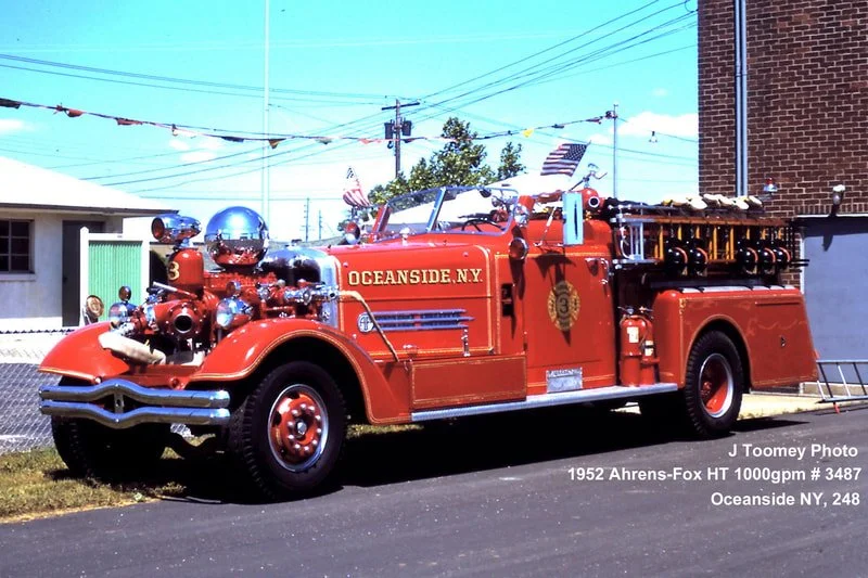 Vintage red fire truck parked on street in Oceanside, NY, with equipment on top and beverages in glass containers.