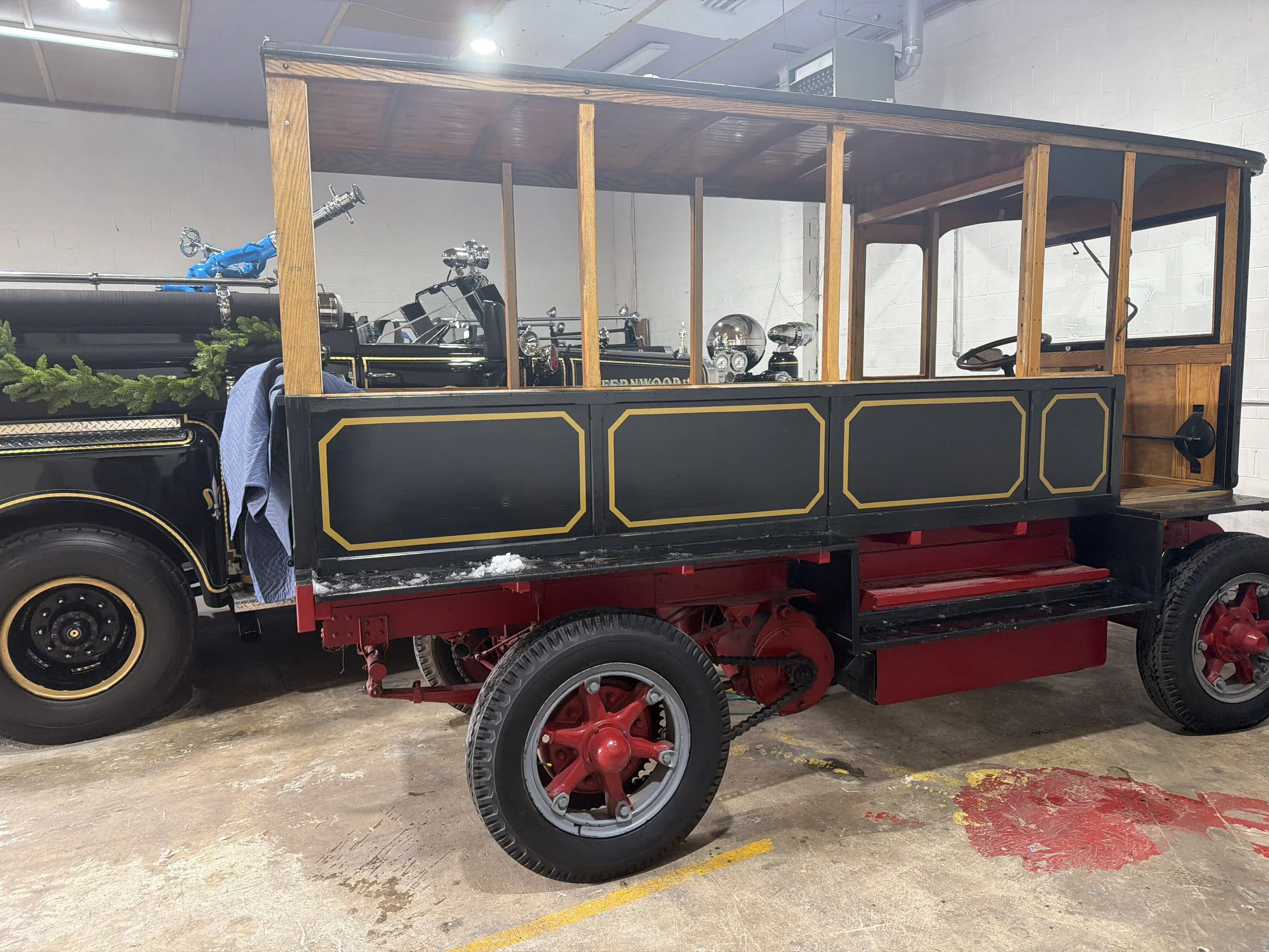 Vintage electric vehicle with a black body, gold trim, and a wooden canopy frame, parked indoors on a concrete floor.
