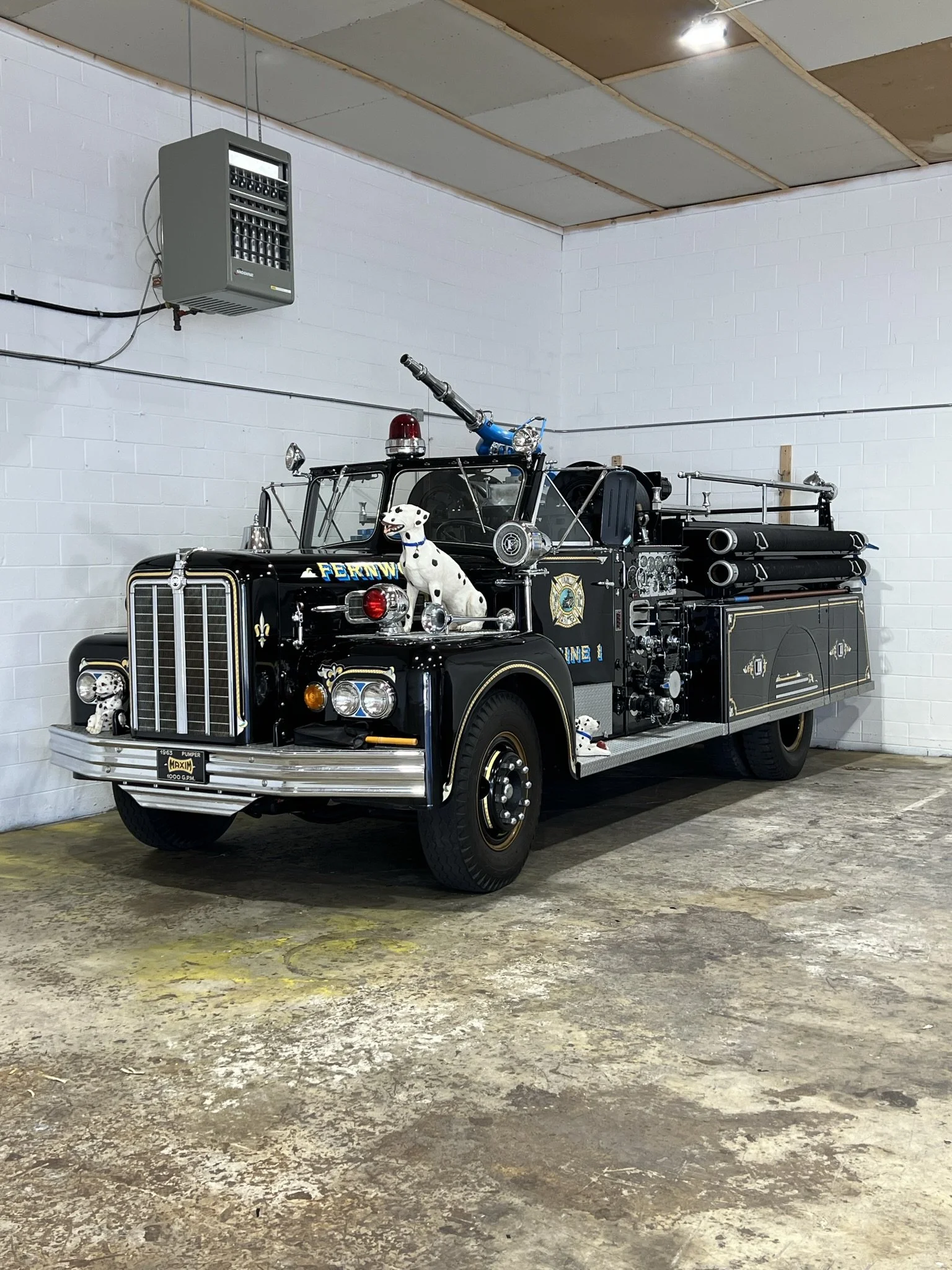 A vintage fire truck decorated with Dalmatian dog figures and firefighting equipment inside a garage.
