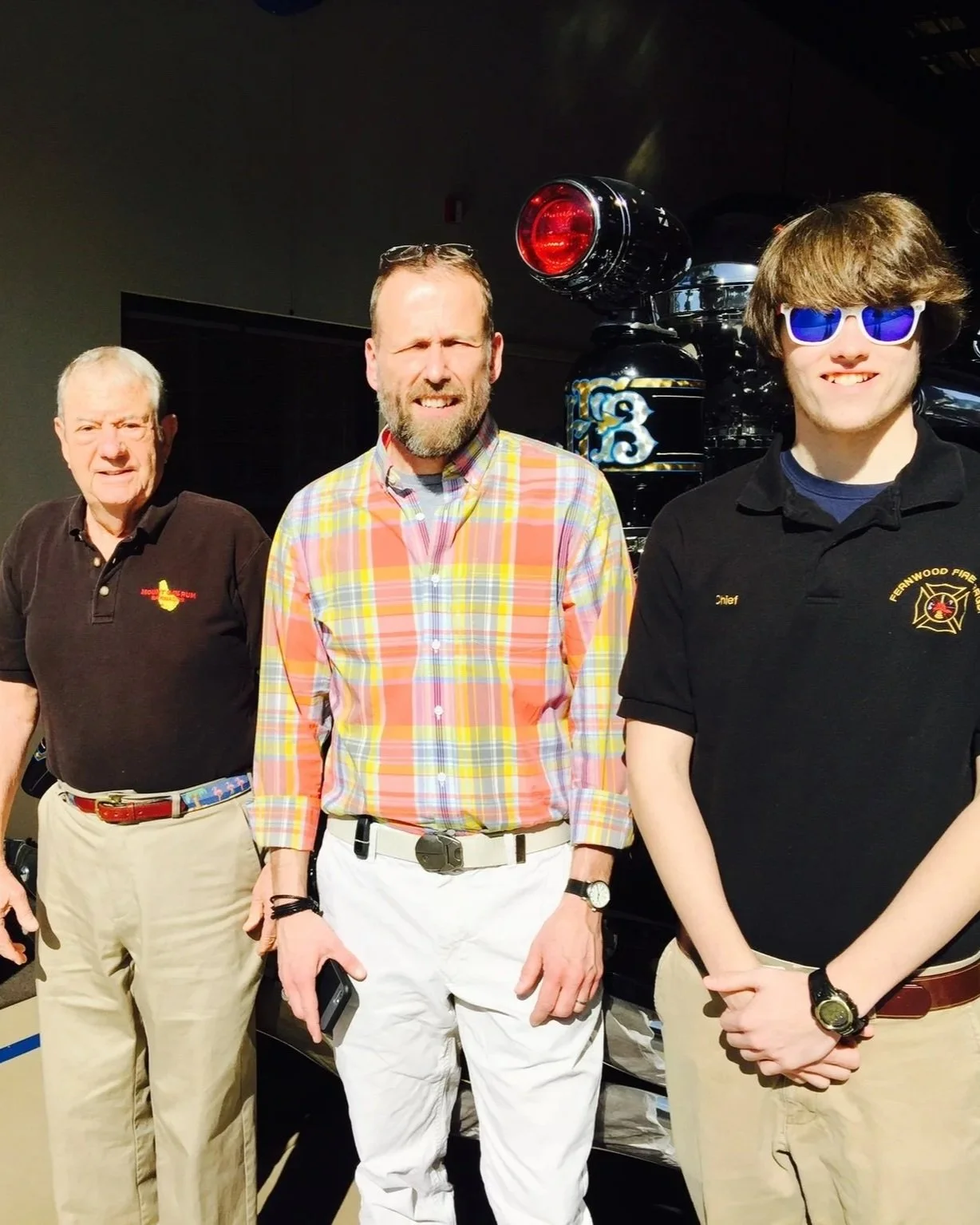Three men standing in front of a fire truck, all wearing uniforms or casual clothing.