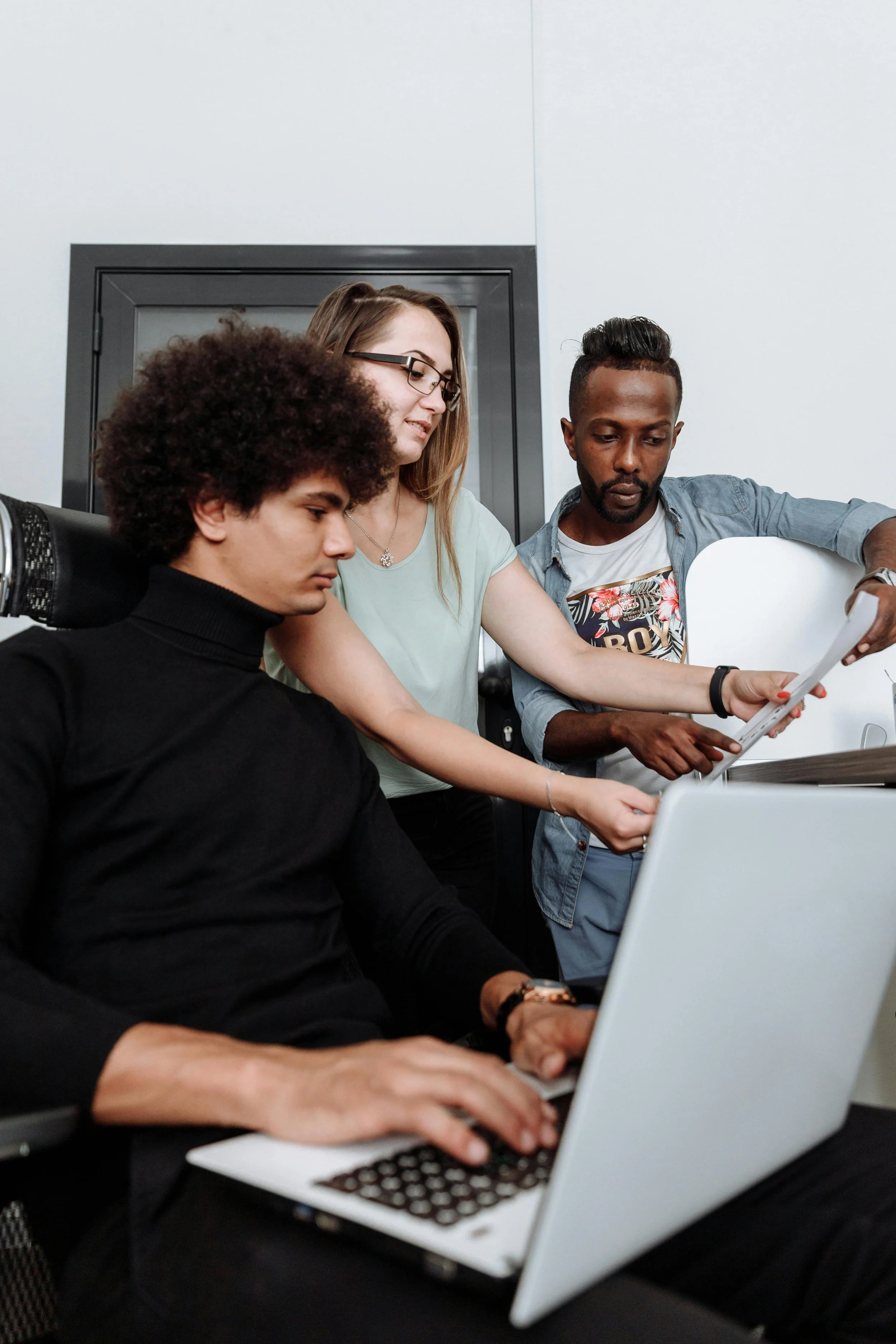 Trois personnes travaillent ensemble autour d'un ordinateur portable dans un bureau, en train de discuter ou de consulter des documents.