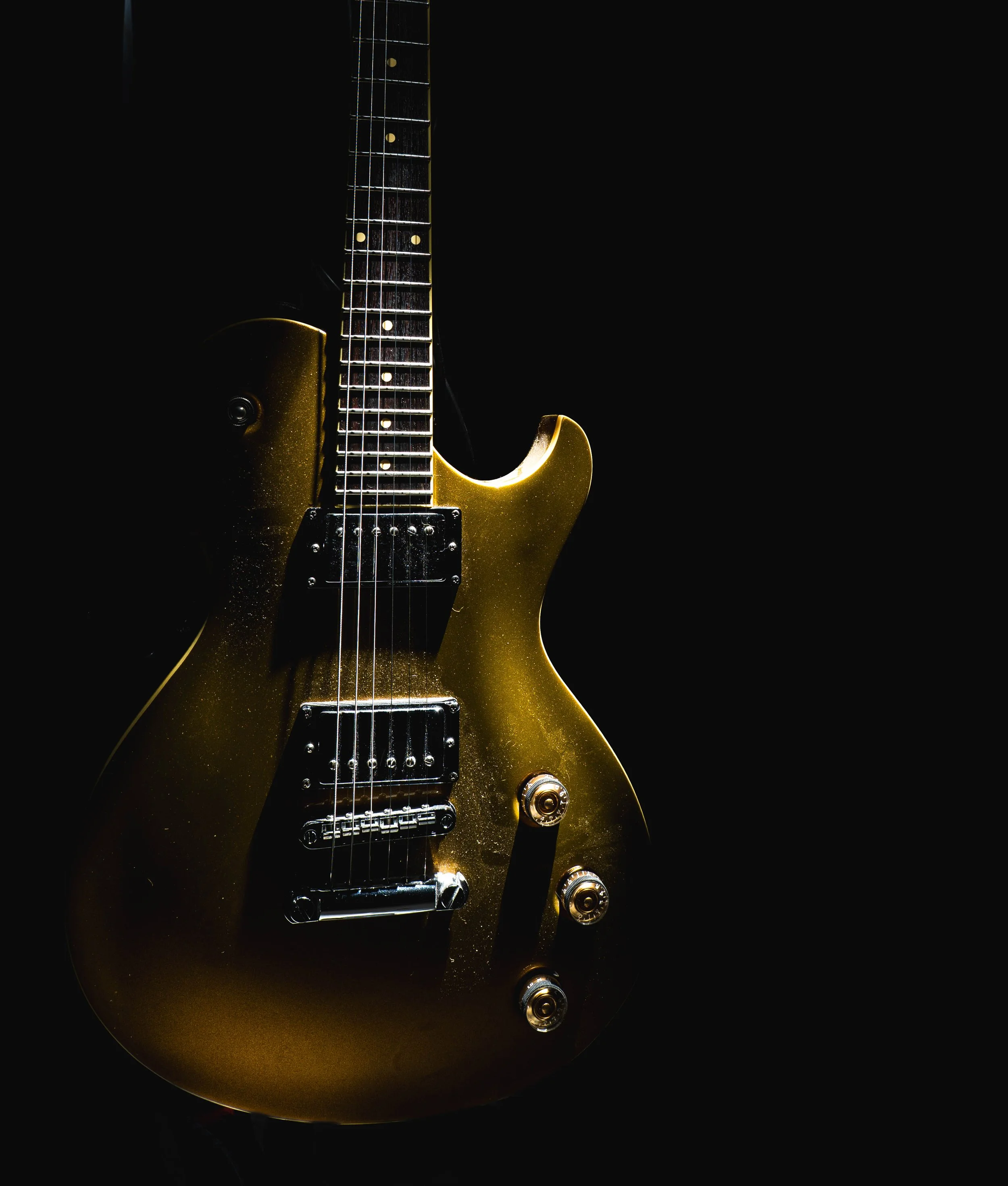 A gold electric guitar with black pickups and knobs, set against a black background.