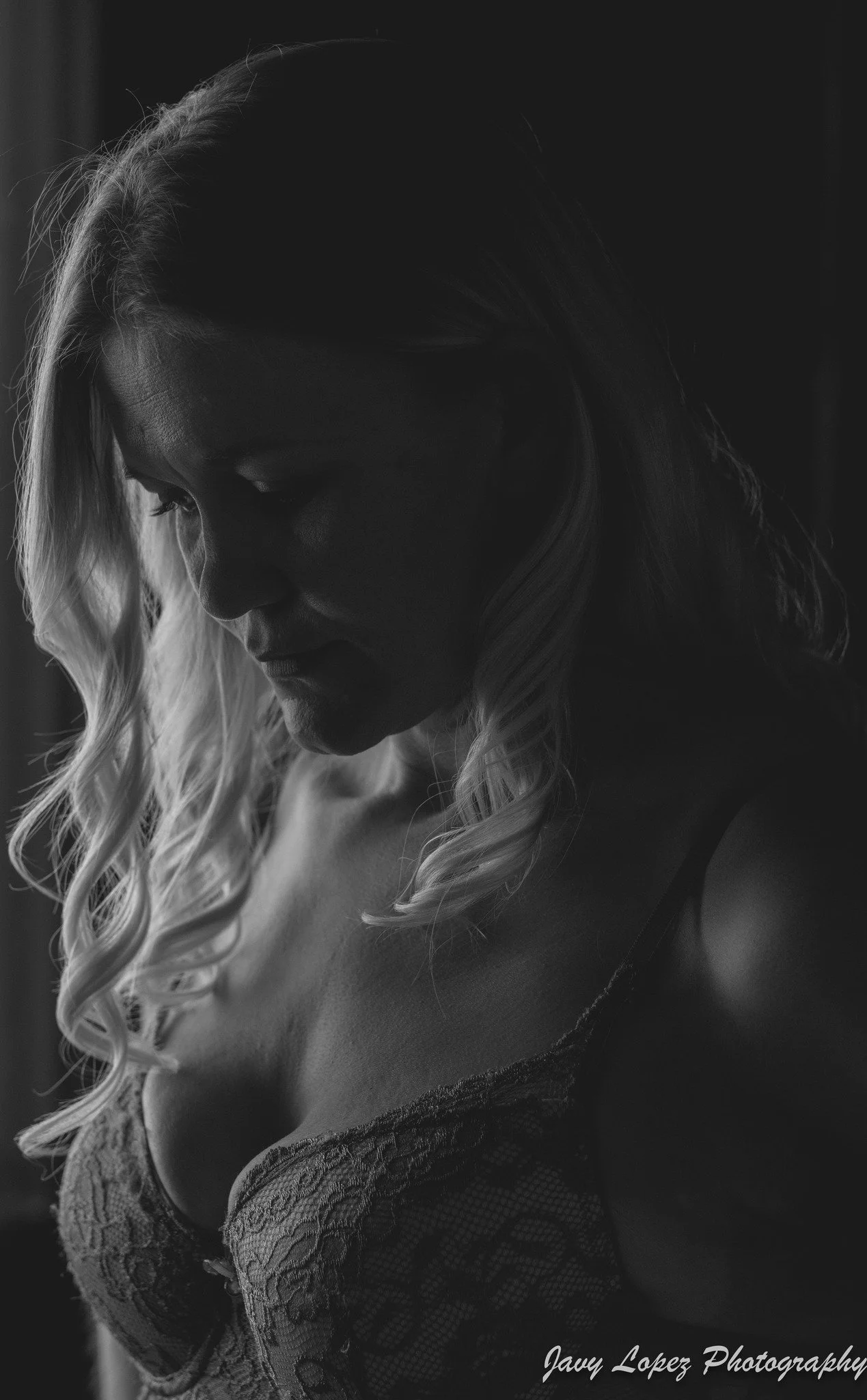 Black and white photo of a woman with long, wavy hair, looking down, wearing a lace top.