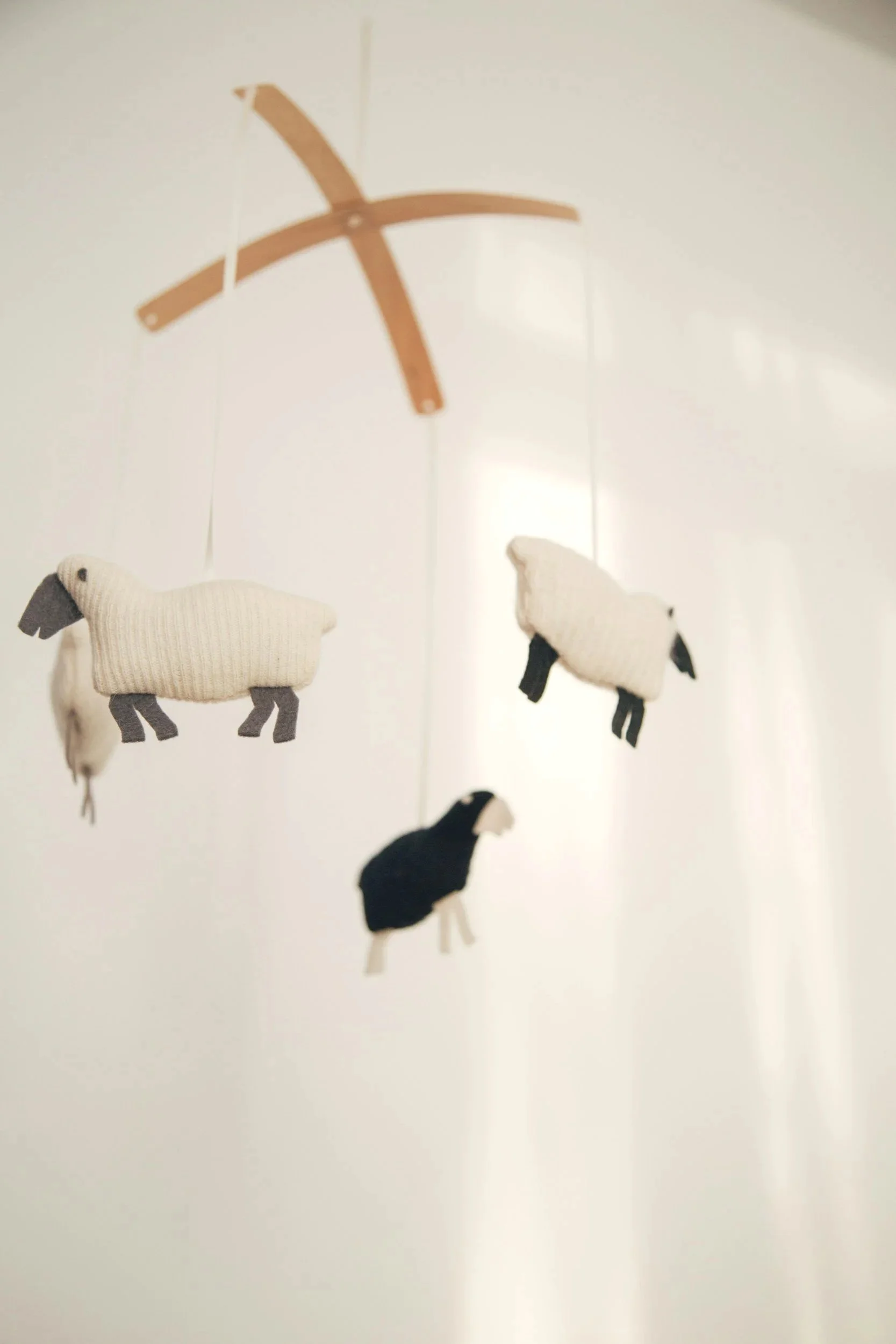A mobile with plush sheep hanging from a wooden crossbar.