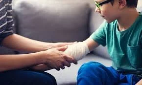 Child with a bandaged hand being held and comforted by an adult.