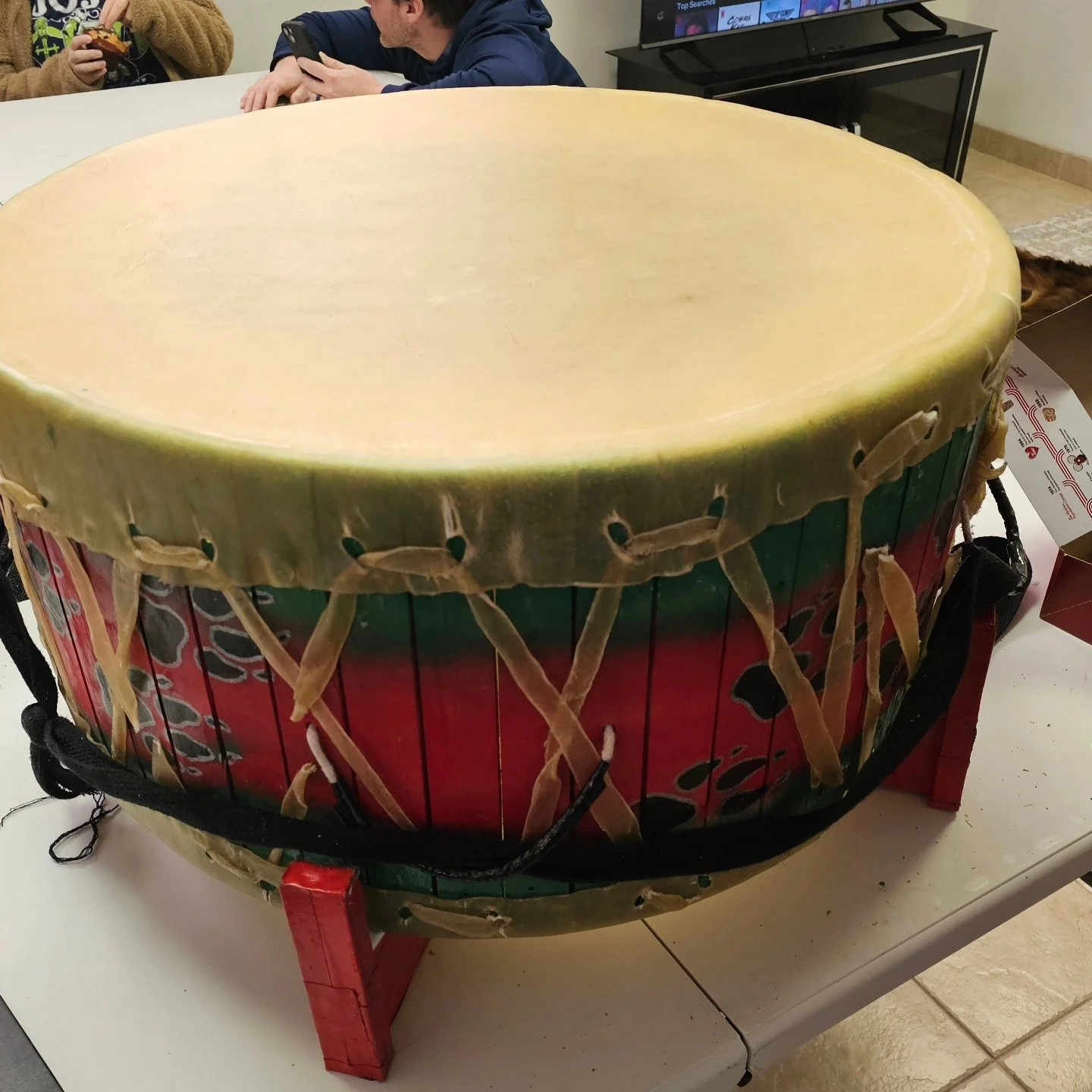 A large, colorful drum with a green, red, and black design around its body, resting on a small table.