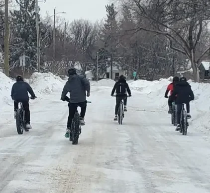 Group of five people riding bicycles on a snowy street in winter.