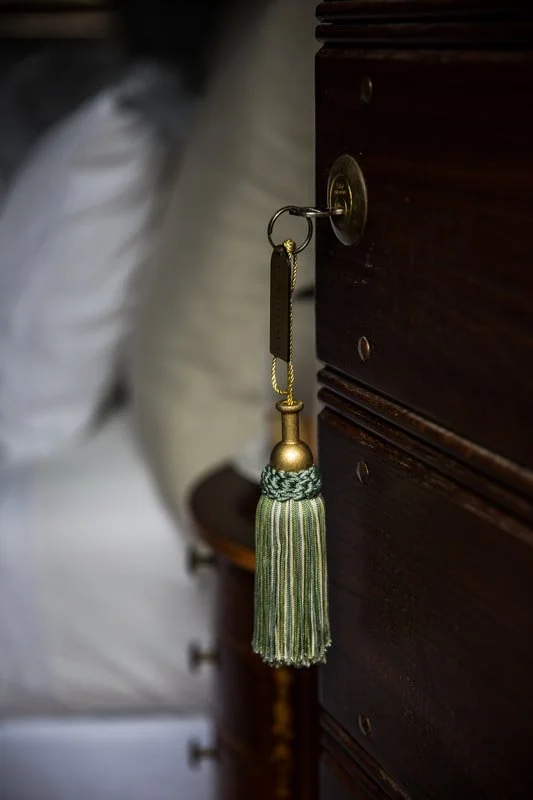 A decorative tassel keychain hanging from a brass door knob on a dark wooden piece of furniture.