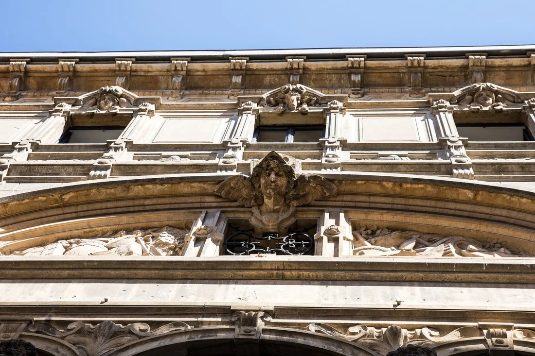 Close-up view of ornate historic building facade with decorative stone carvings and a sculpted face with wings.