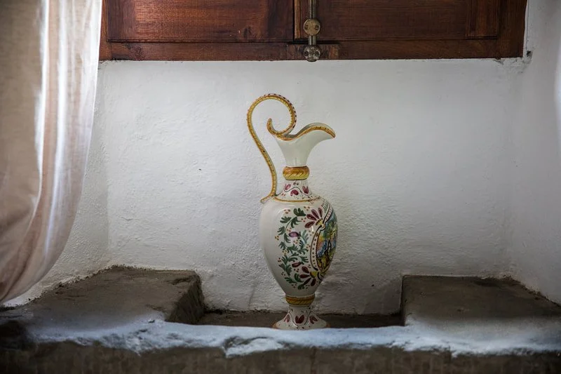 Decorative ceramic vase with floral and mythical creature designs, placed in a recessed stone nook against a white wall, with a wooden cabinet above.