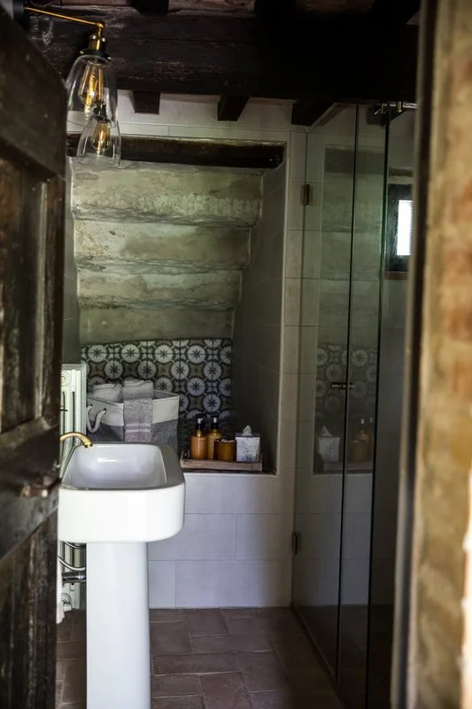 Small bathroom with a pedestal sink, glass shower enclosure, and decorative tile wall.