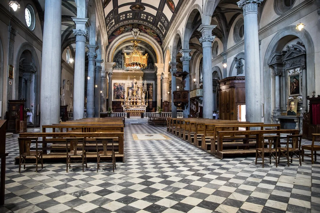 Interior of a historic church with high vaulted ceilings, columns, wooden pews, and an ornate altar at the front.